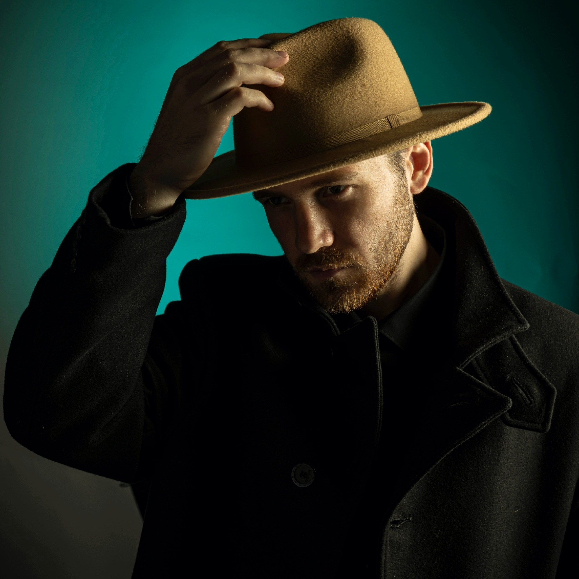 Портрет мужчины со щетиной в черном пальто и бежевой шляпе