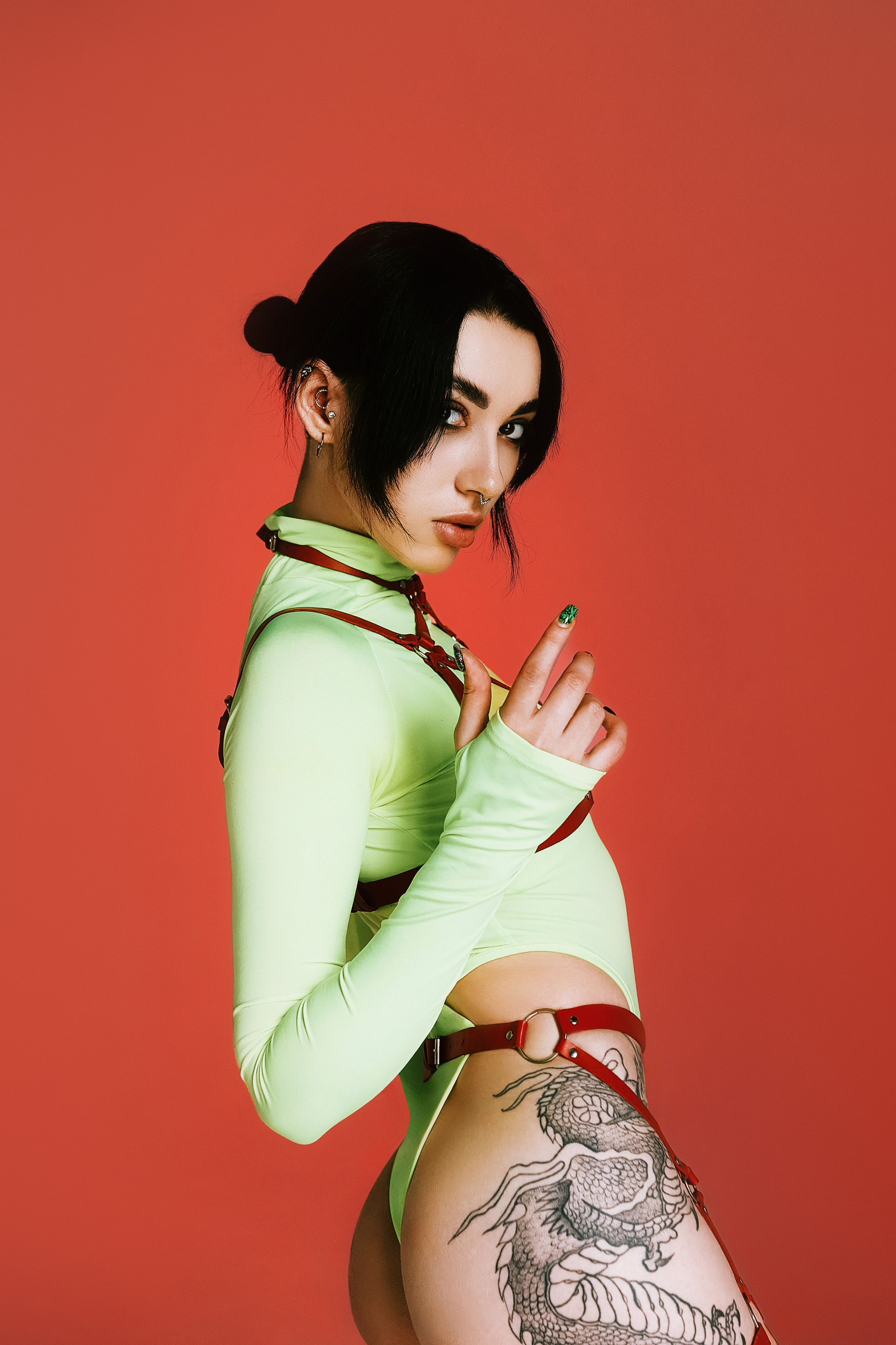 Фэшн фотосессия на красном студийном фоне с татуированной моделью в боди, портупее и гартерах