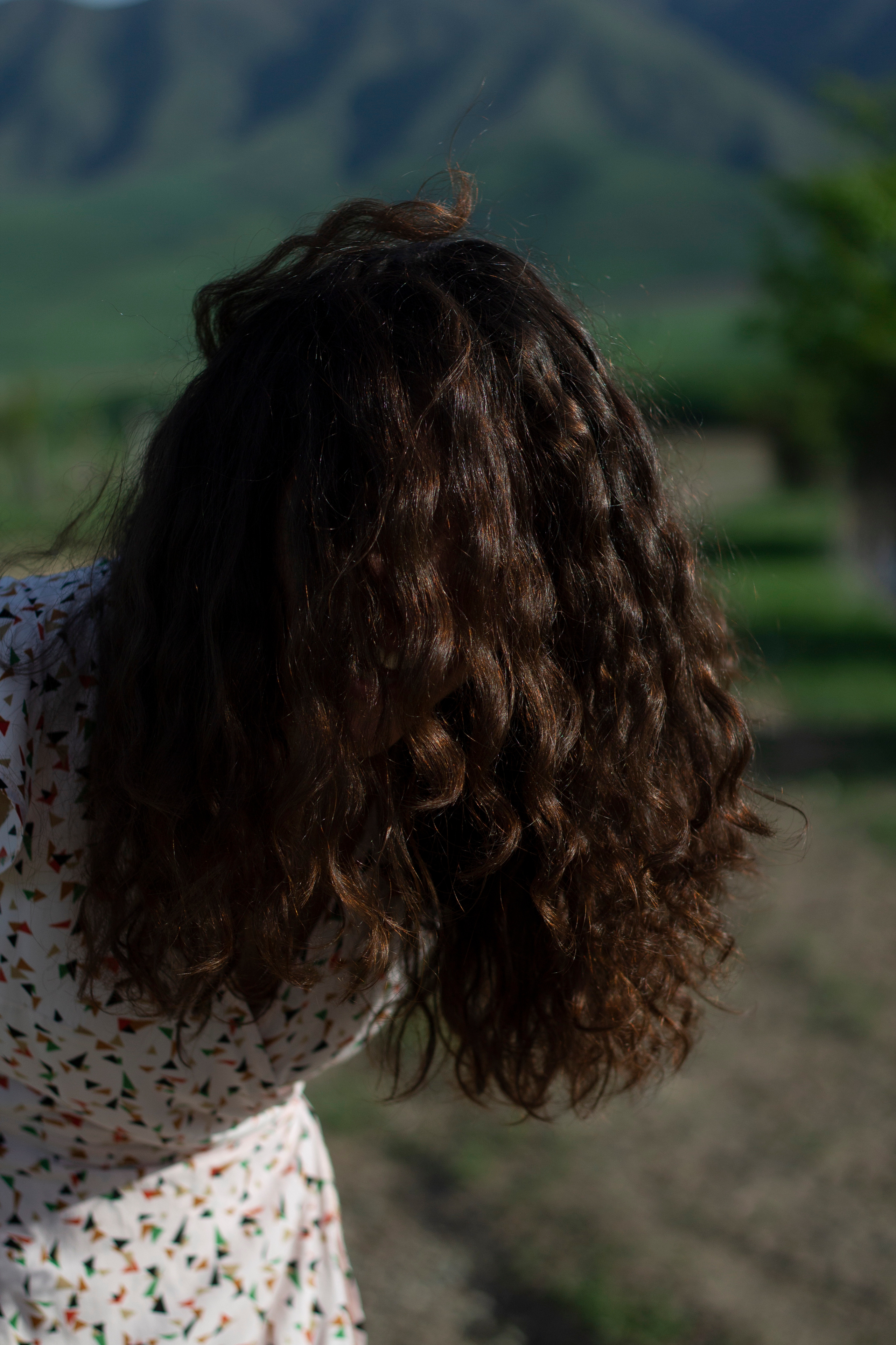 В горах девушка перекинула длинные кудрявые волосы на лицо и улыбается