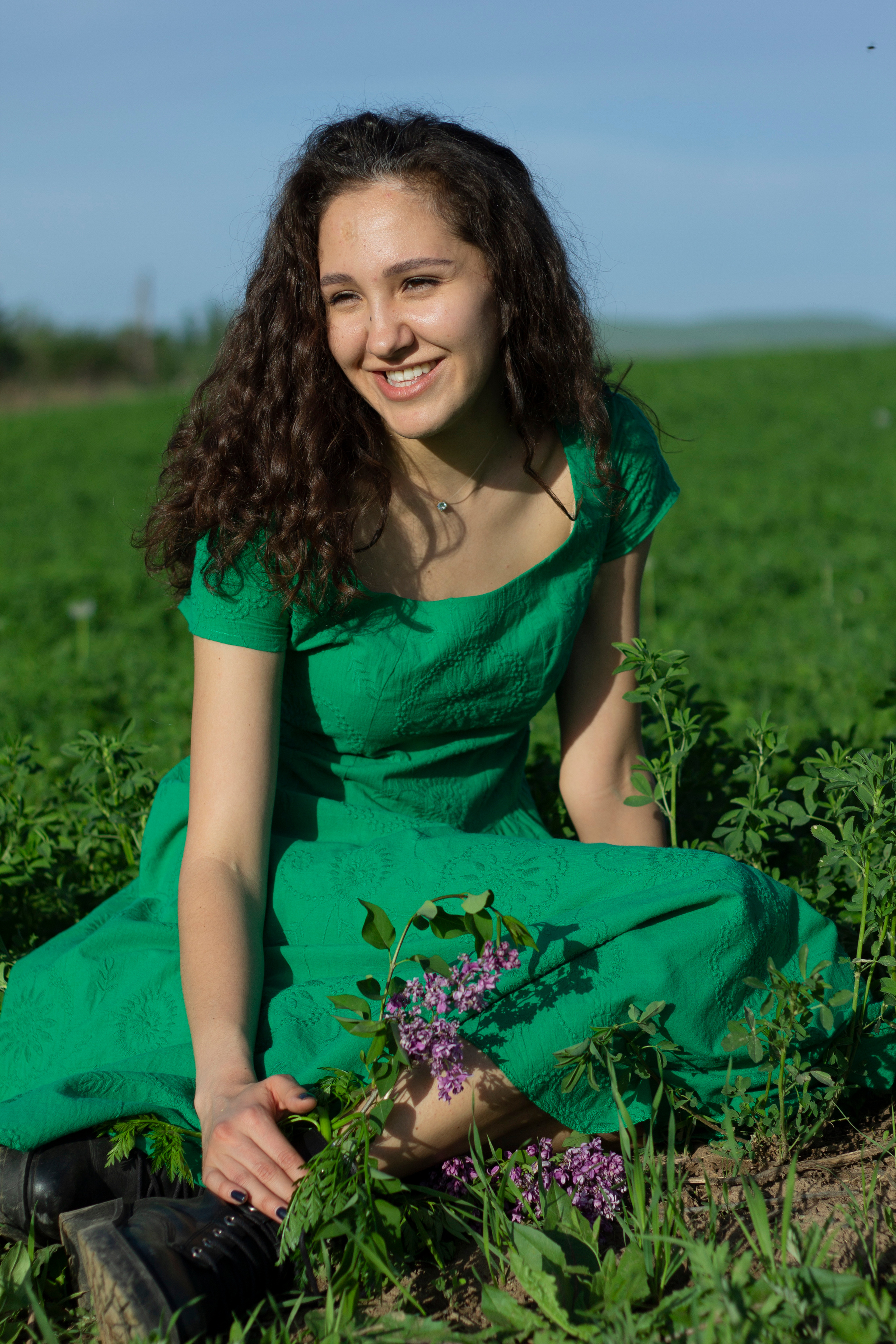 Девушка в зеленом платье сидит в поле клевера и улыбается