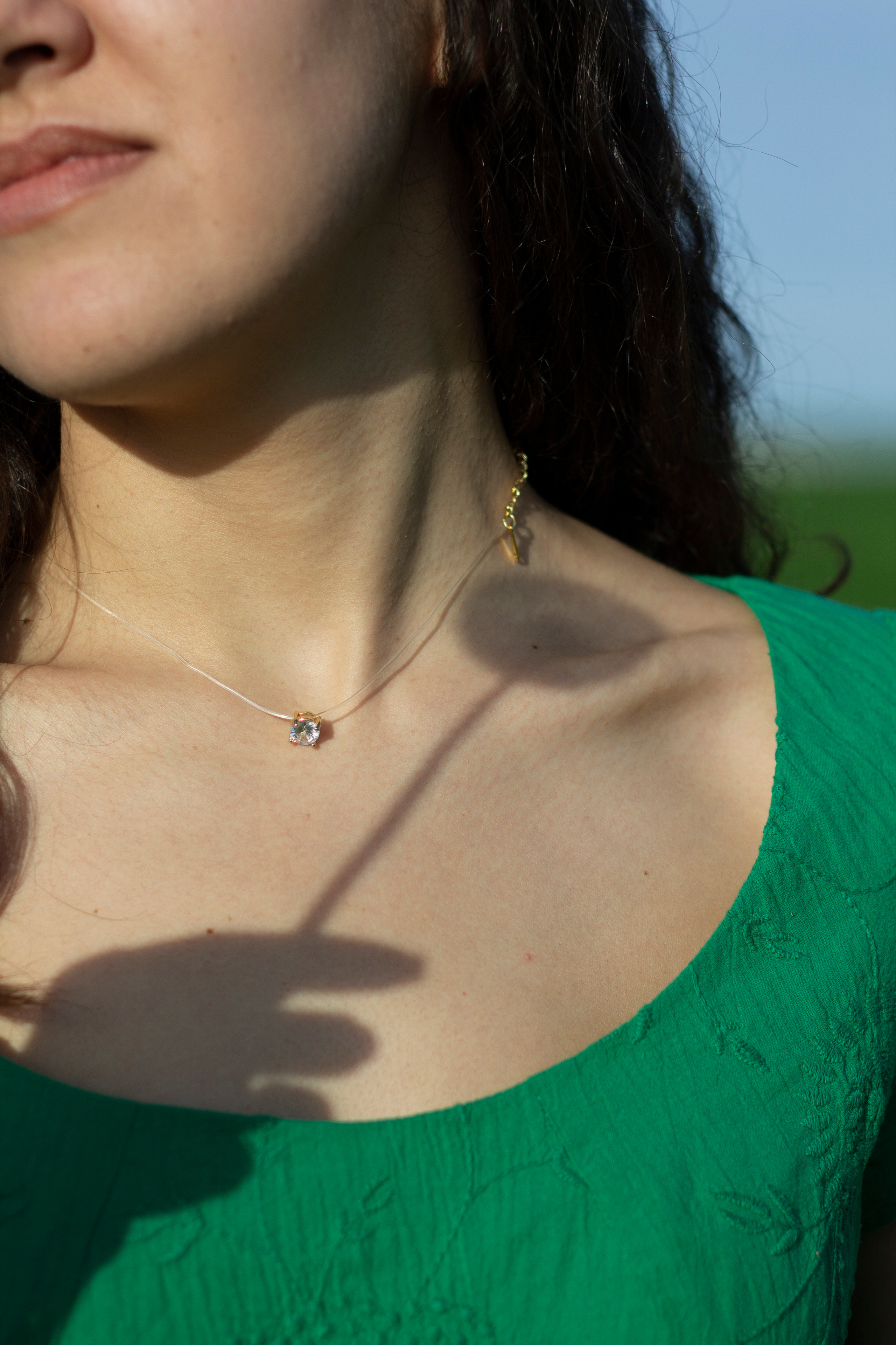 Тень от руки держащей одуванчик падает на шею девушки в зеленом