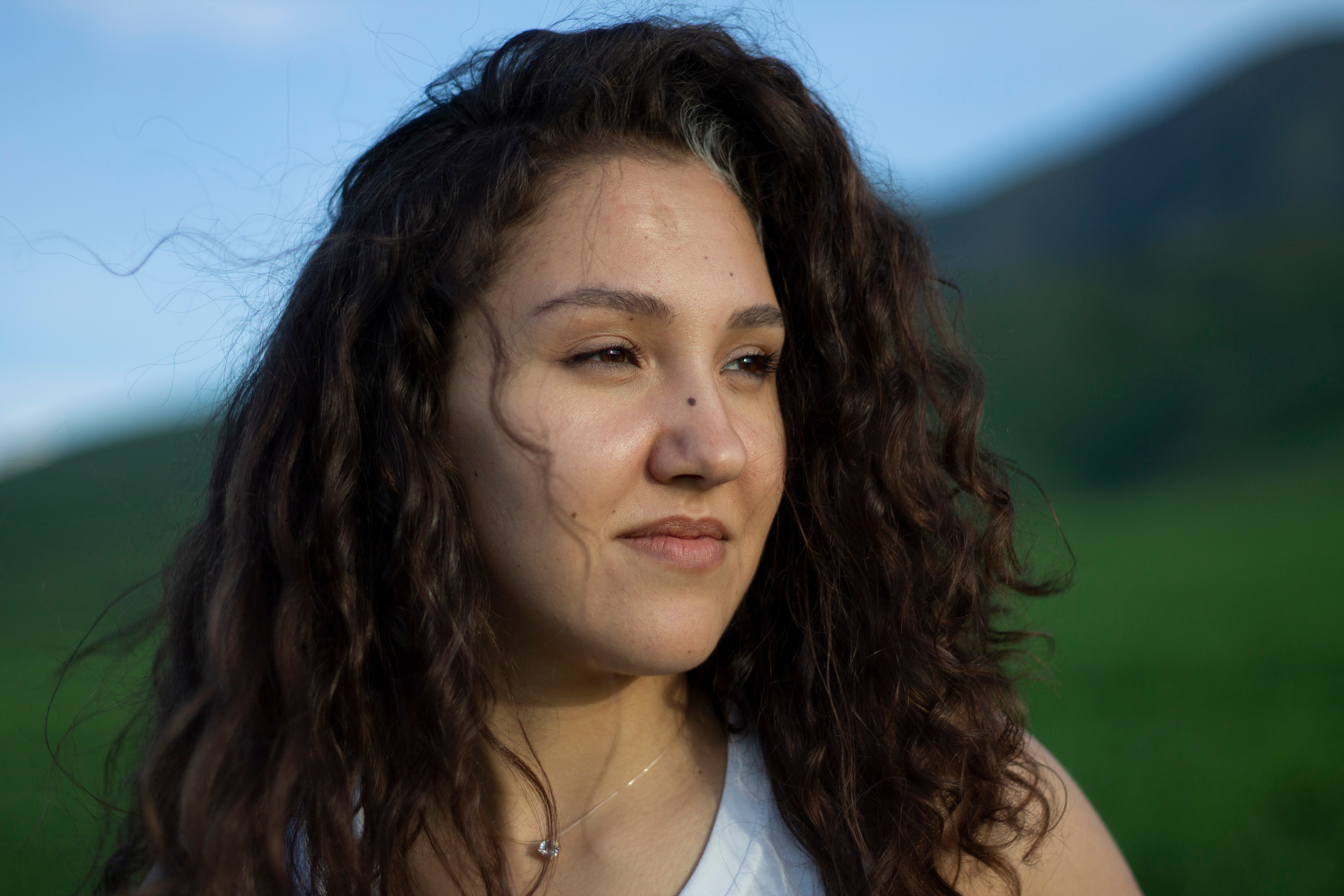 Девушка с кудрявой головой на фоне гор смотрит на закатное солнце