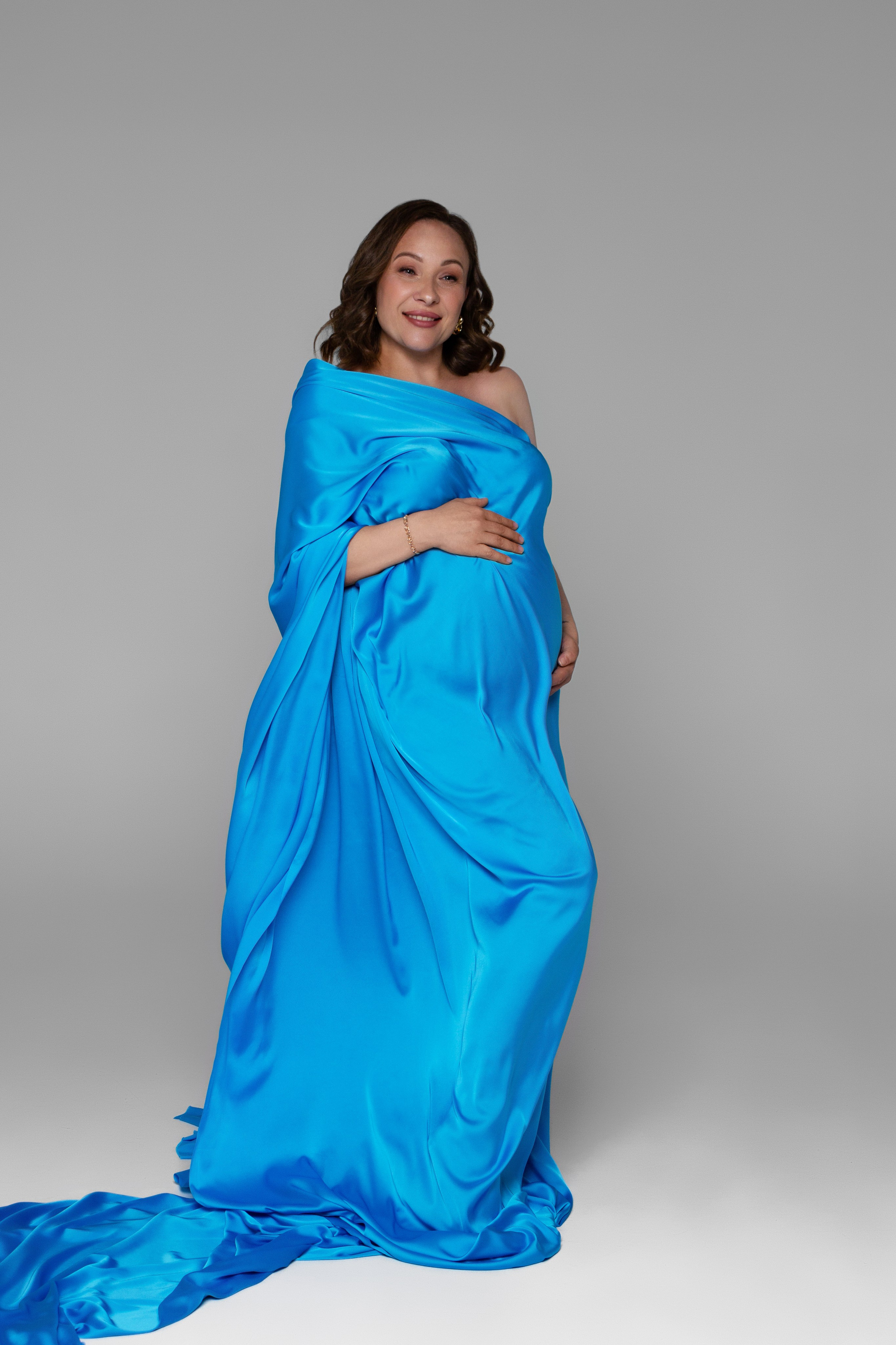 беременная девушка в шелковой голубой ткани, которая развивается за спиной 