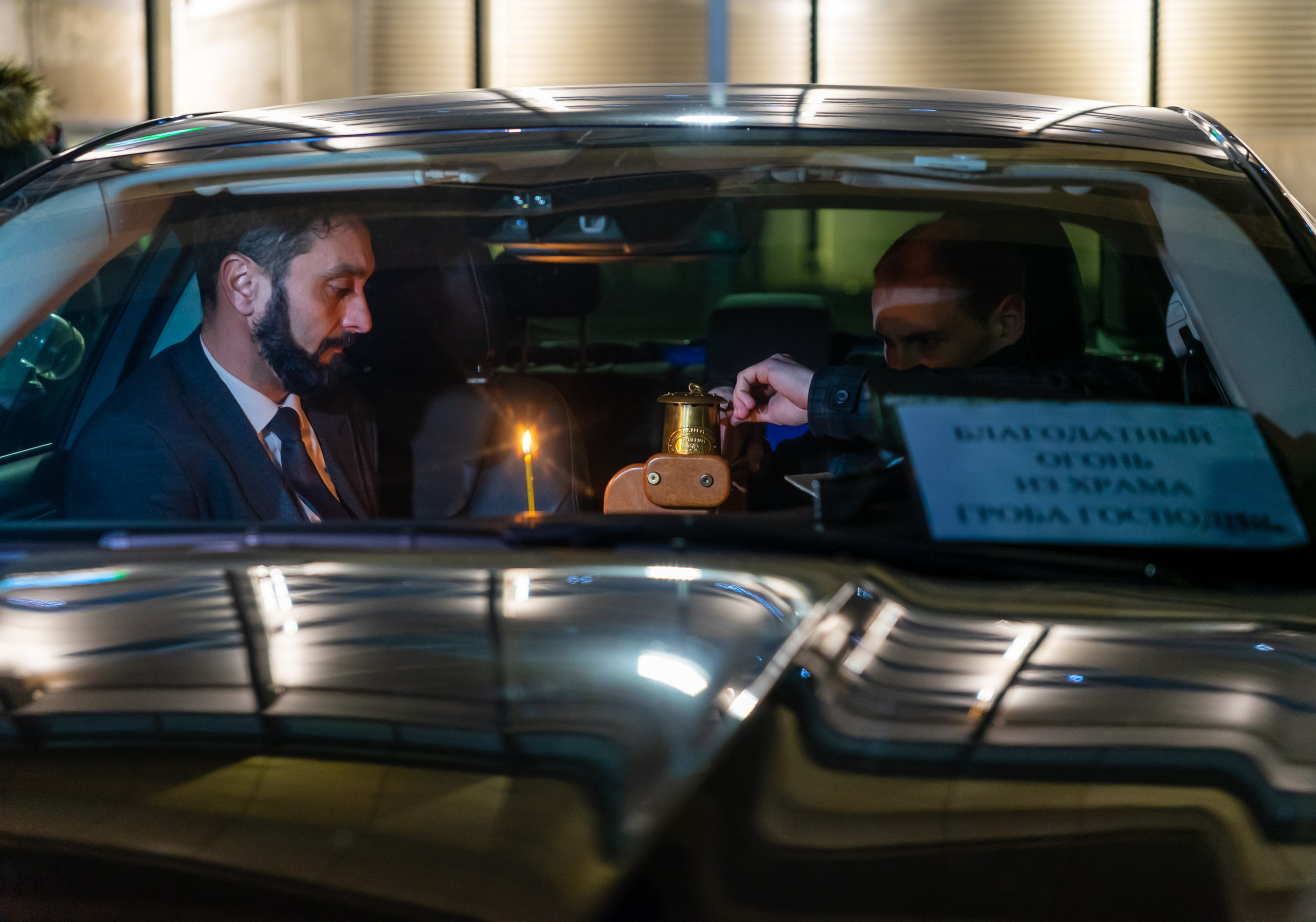 Передача Благодатного огня 2022 в автомобиле после прибытия в Пулково: бородатый мужчина и священник с лампадой из Храма Гроба Господня, ночная съёмка Санкт-Петербург, фотограф Мальцев Евгений evrednix.ru.