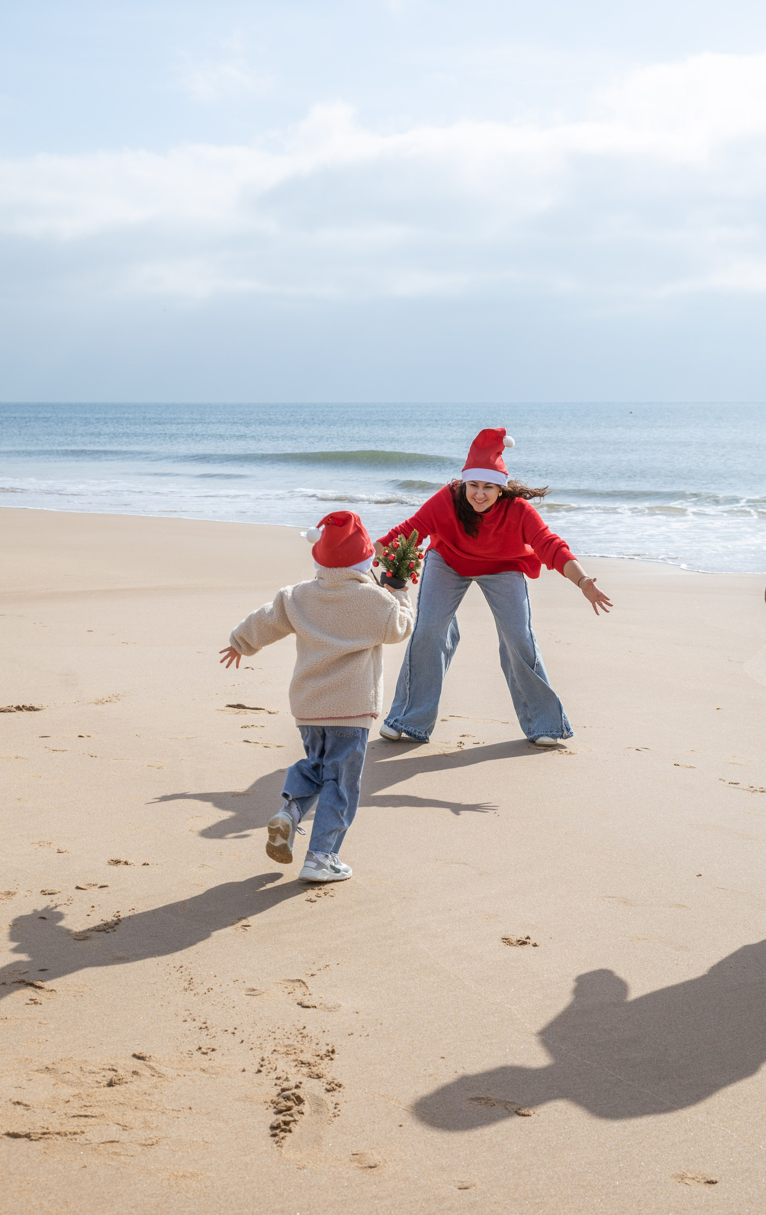 Mum, dad, and daughter laughing together as the waves touch their feet. A joyful moment by the ocean, as the family plays on the shore