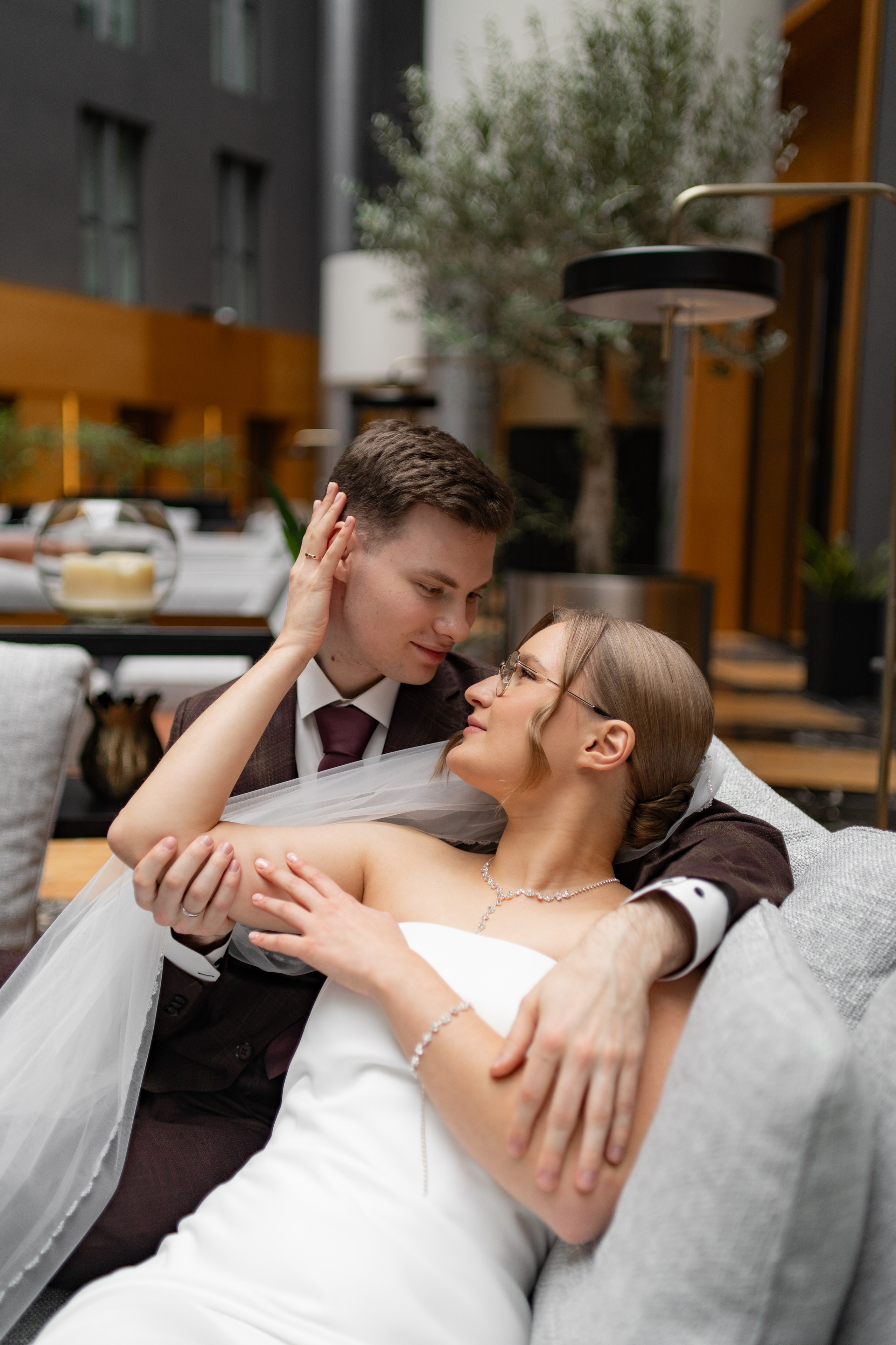 Жених обнимает невесту на серых креслах в атриуме в отеле Гамма на свадебной фотосессии 