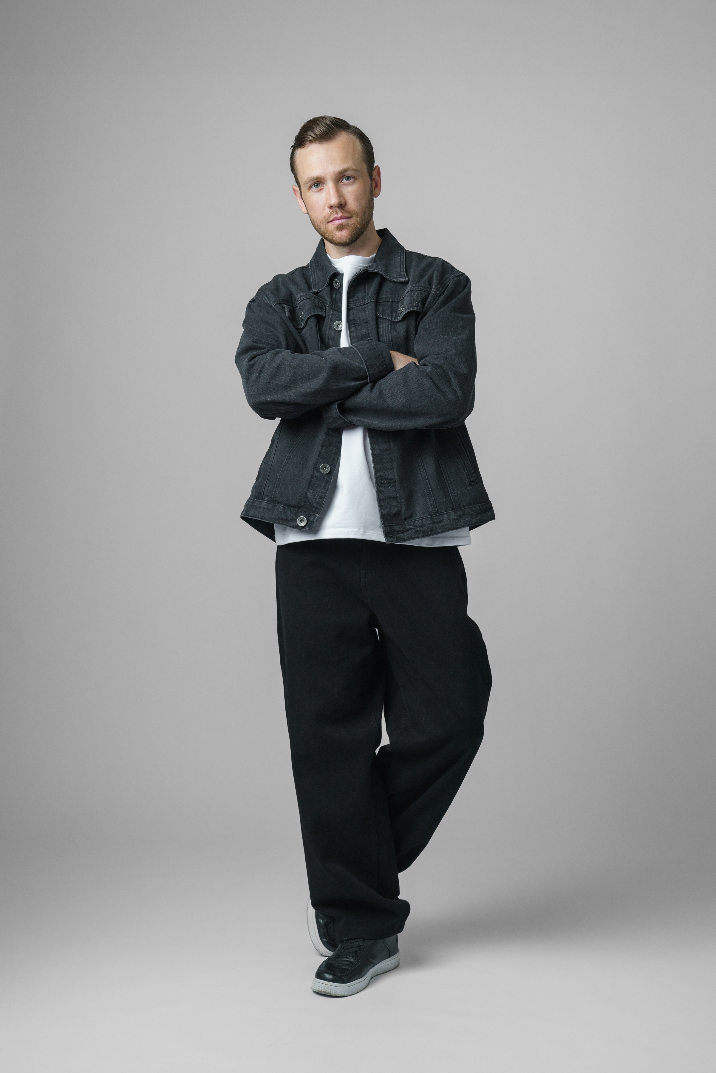 Мужчина с короткой щетиной в джинсовой куртке и темных больших штанах