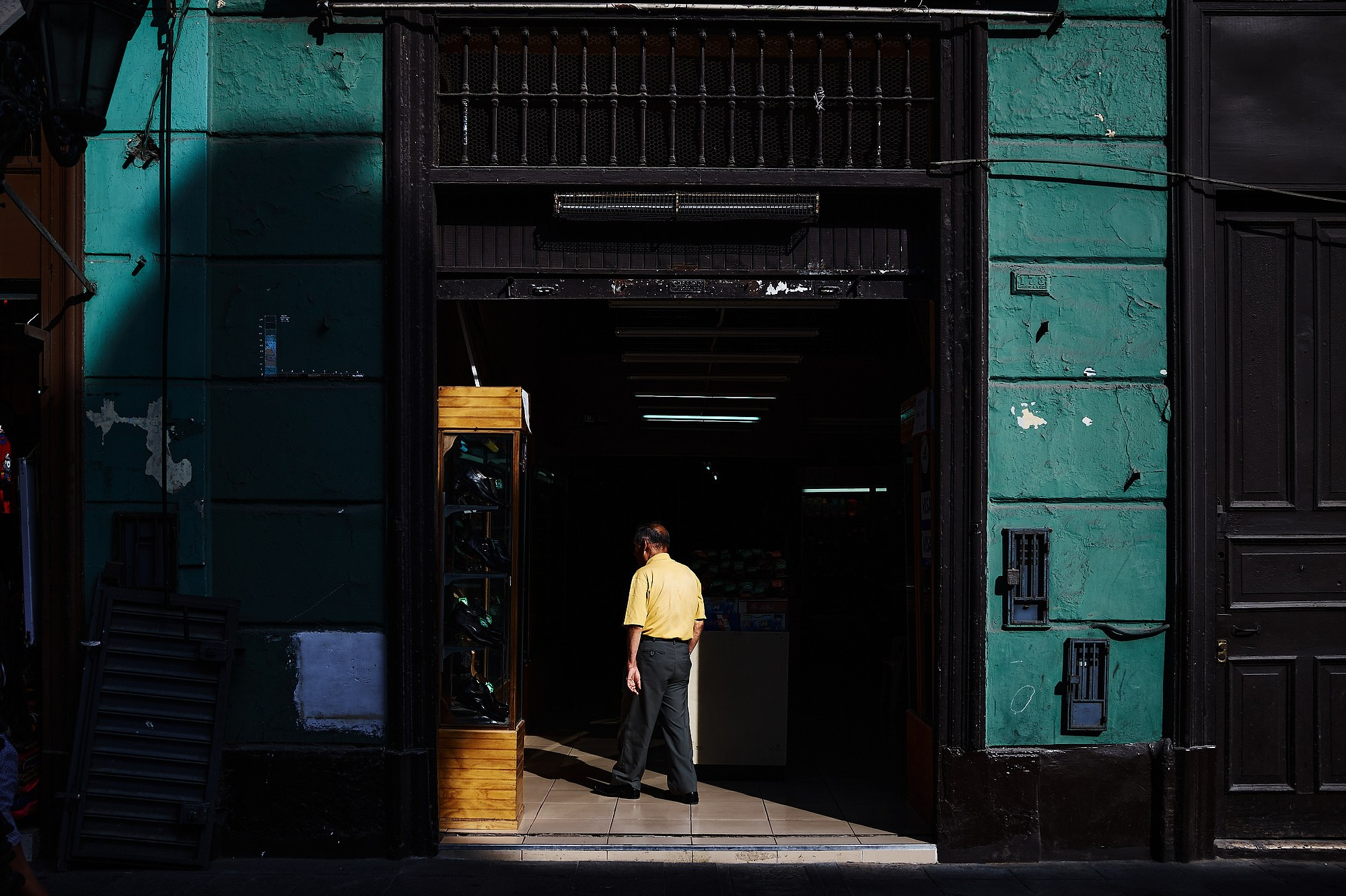 Работа со светом и цветом в уличной фотографии. Одинокая фигура человека в желтом становится композиционным центром, разделяя границу между слепящим солнцем и глубокой темнотой проема