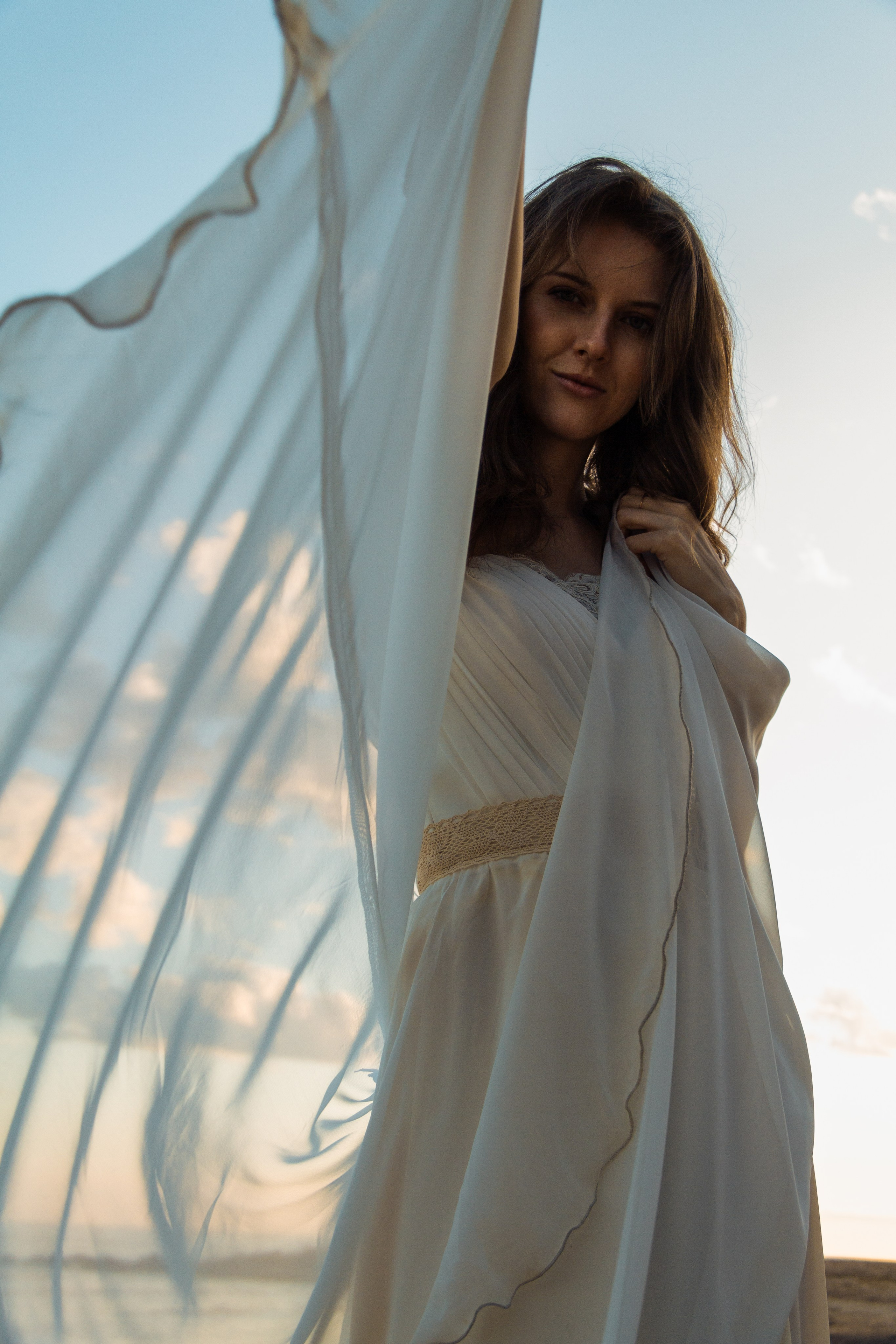 Девушка в белой воздушной ткани. Ветер на берегу моря. Красивая девушка на берегу моря.