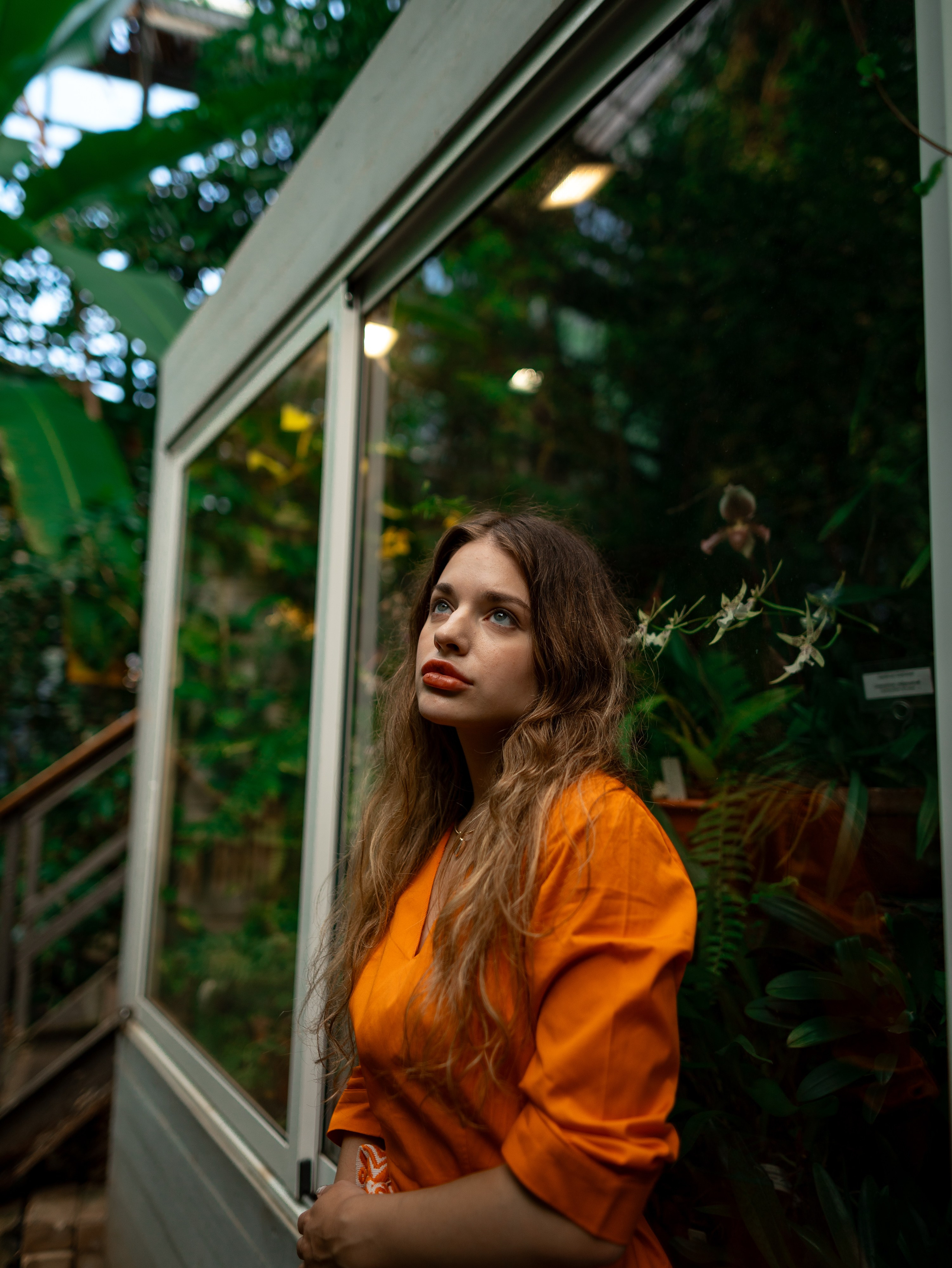 Девушка в оранжевом платье стоит на фоне зелени