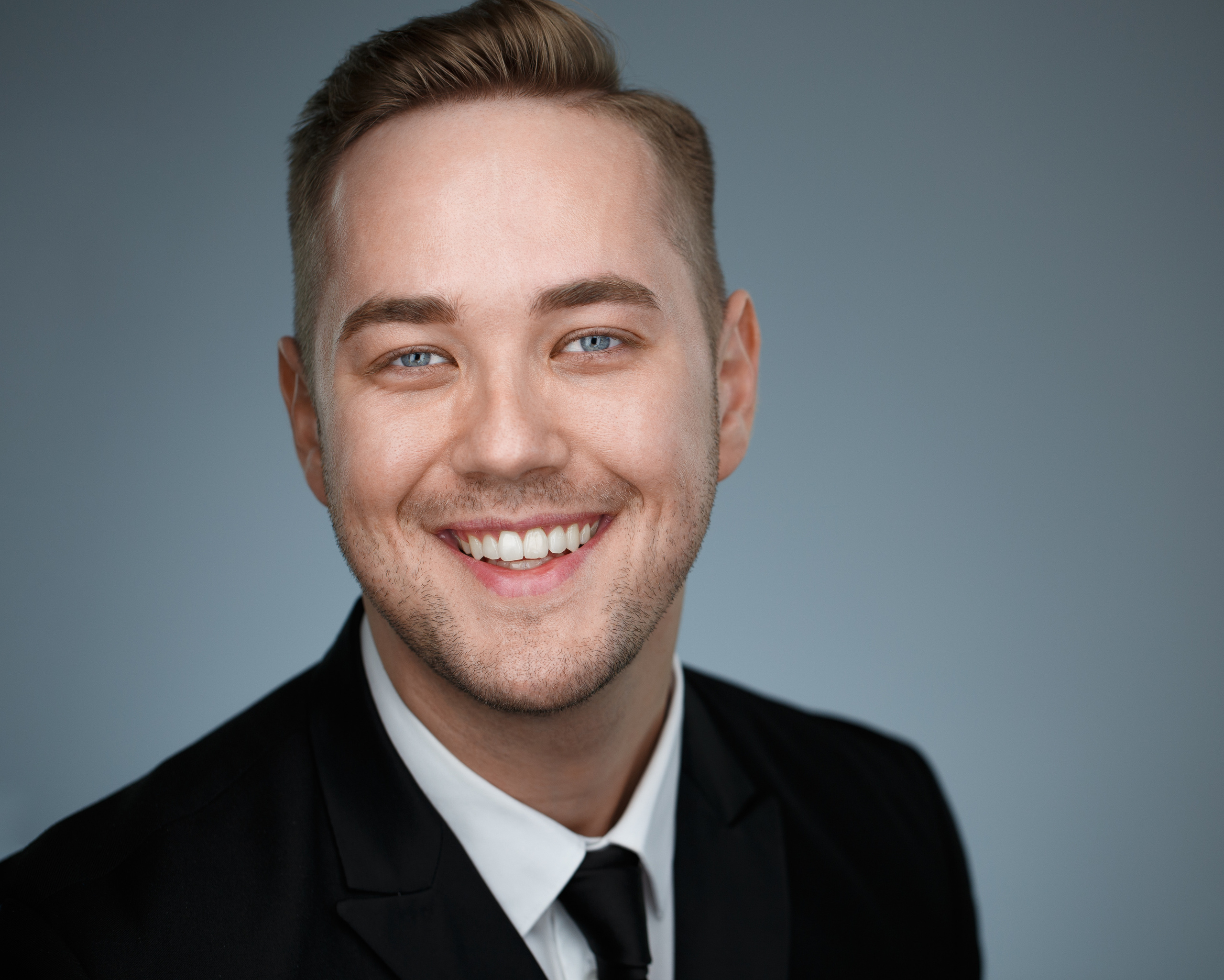 Хедшот. Деловой портрет улыбающегося молодого человека на сером фоне.