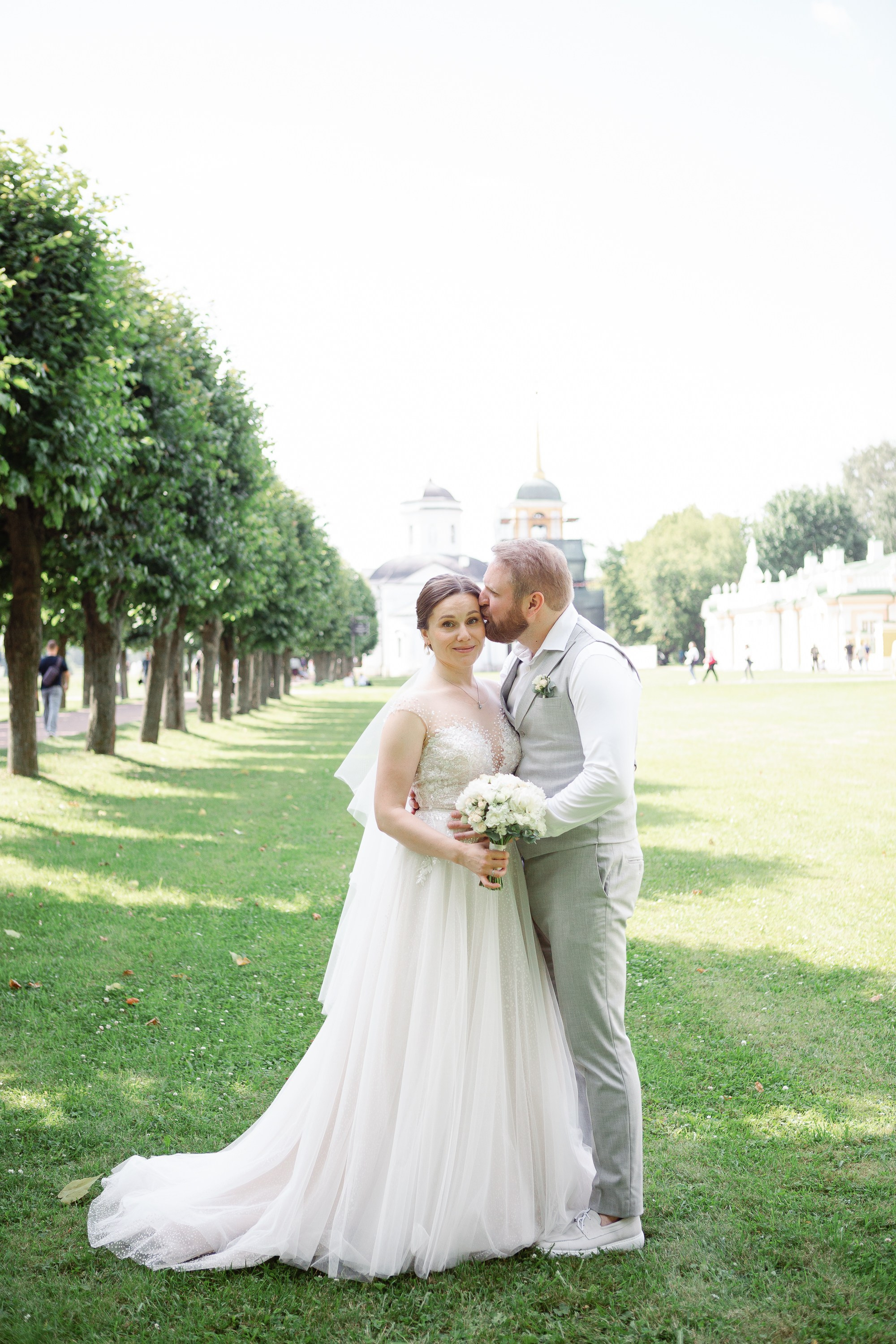 Жених обнимает и целует невесту в парке в Москве.