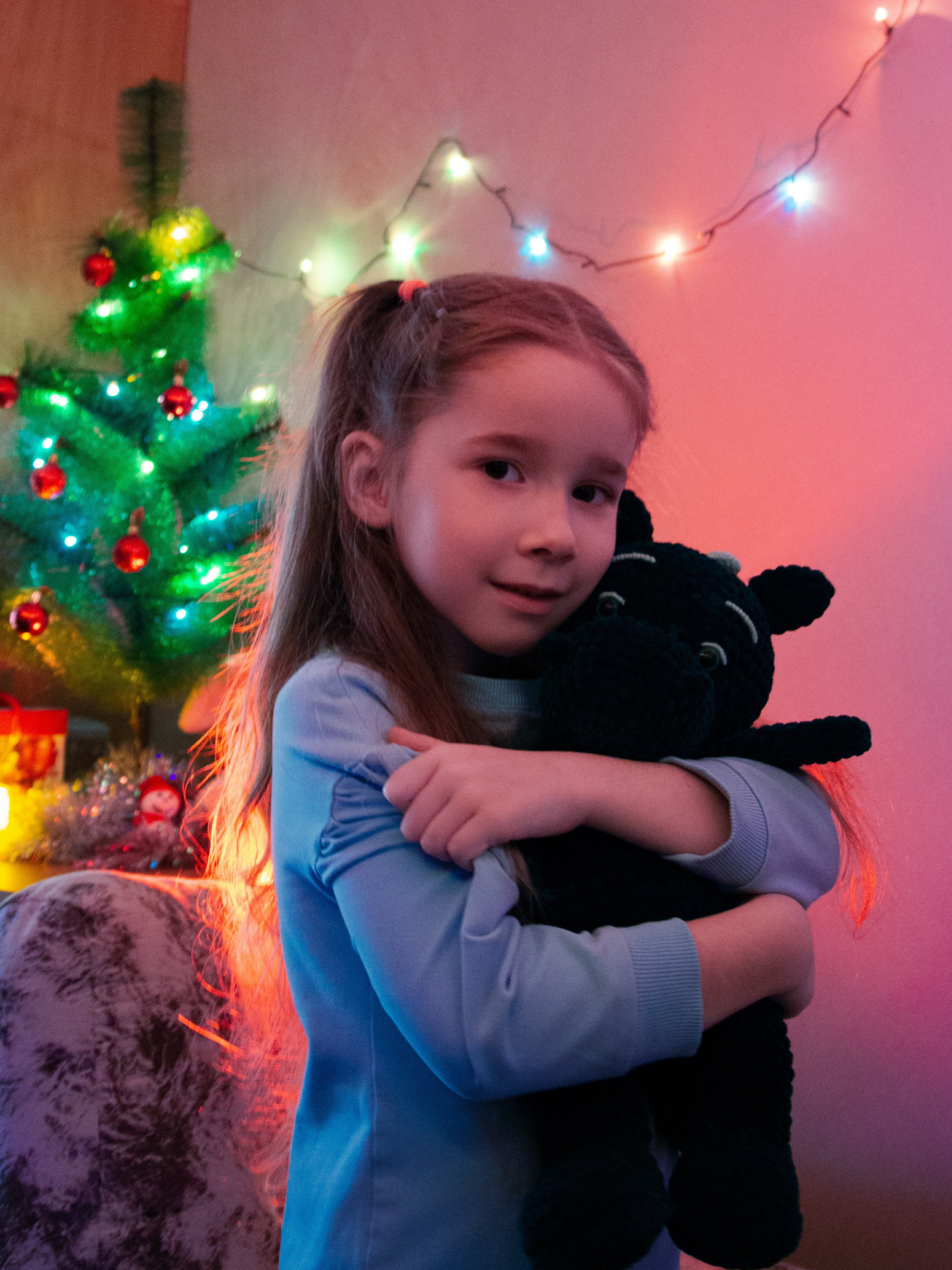 Девочка в новогодней обстановке обнимает игрушку