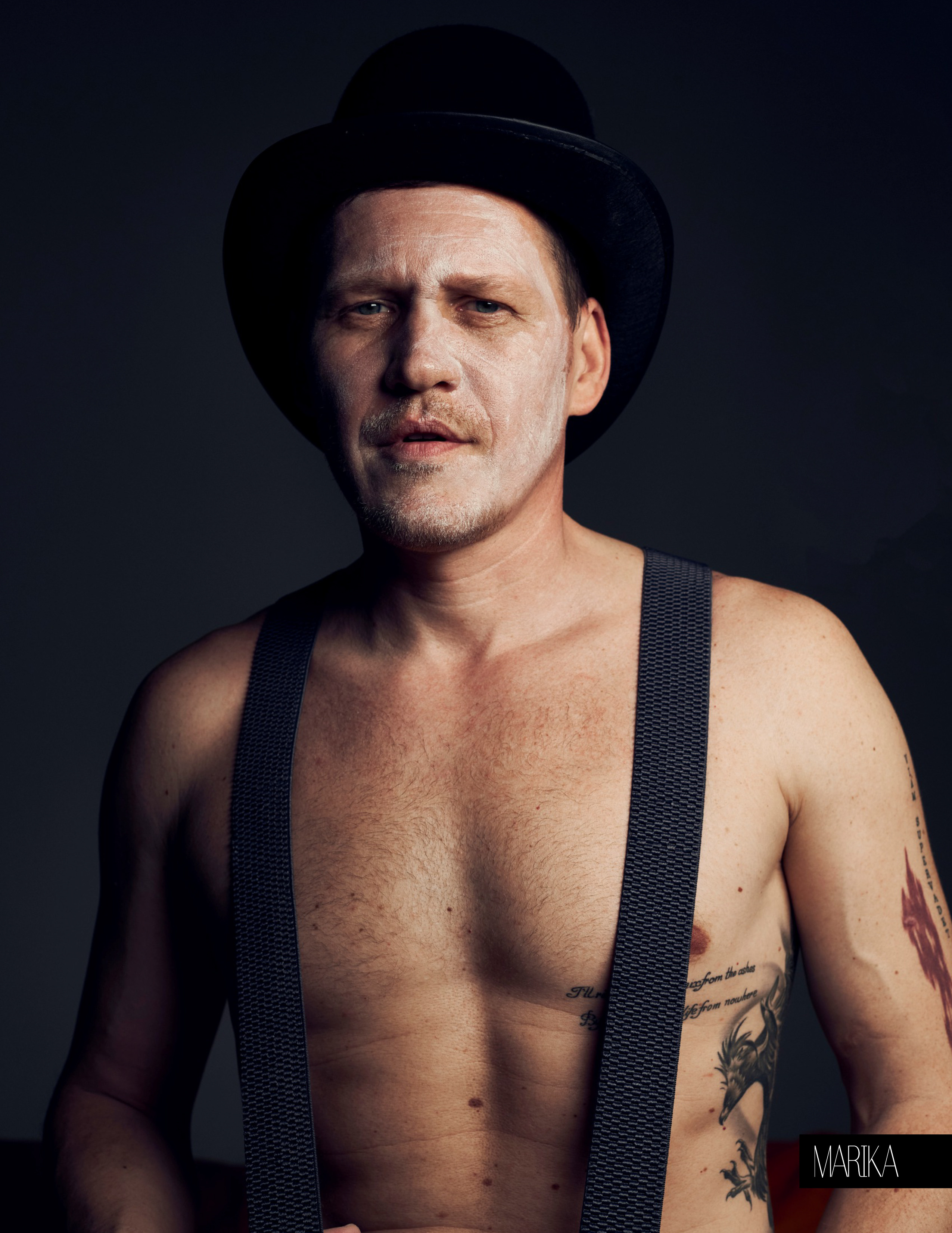 Портрет мужчины с татуировками в черном цилиндре и подтяжках на голое тело, лицо раскрашено белым гримом