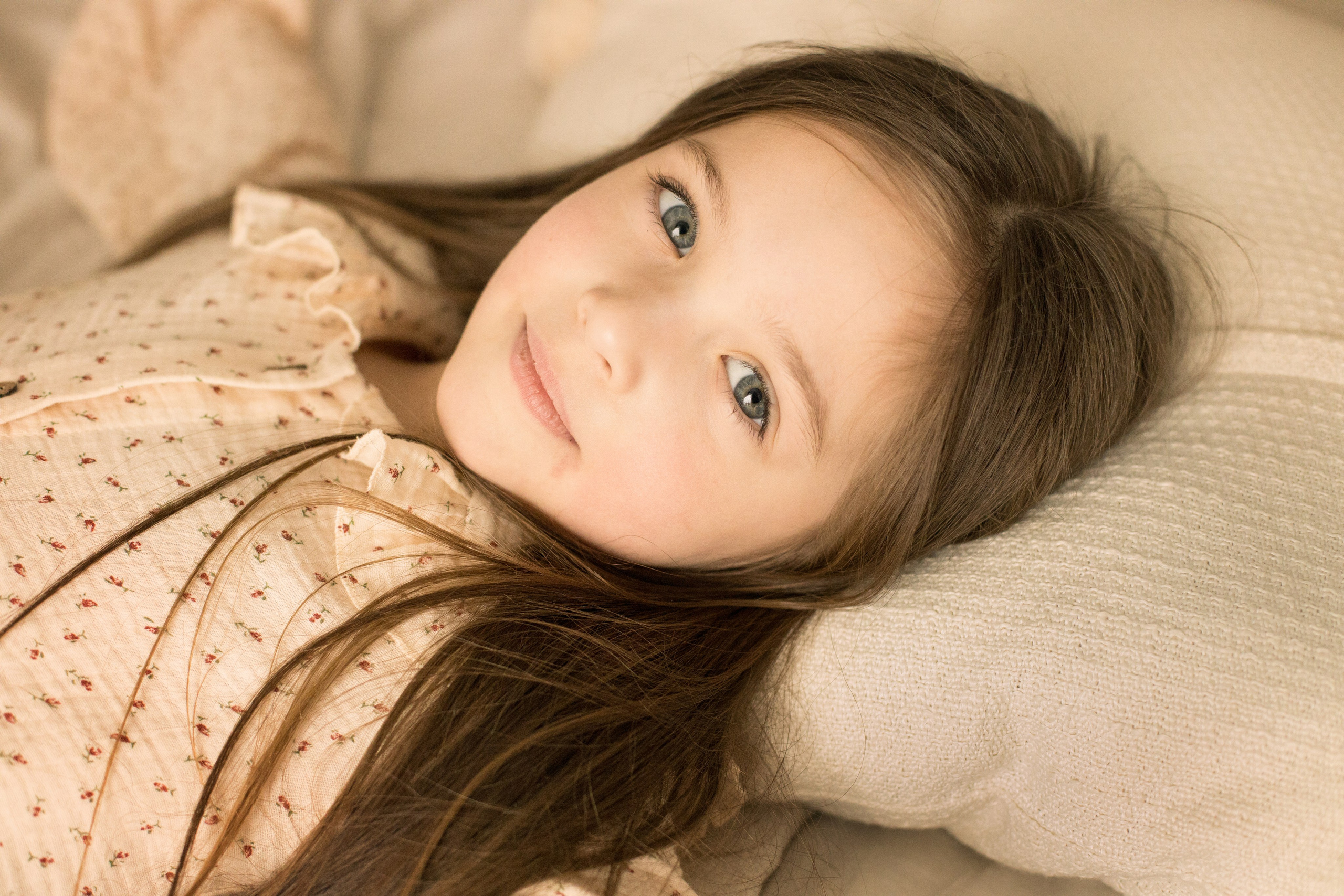 Портрет девочки с голубыми глазами и каштановыми волосами лежа на подушке