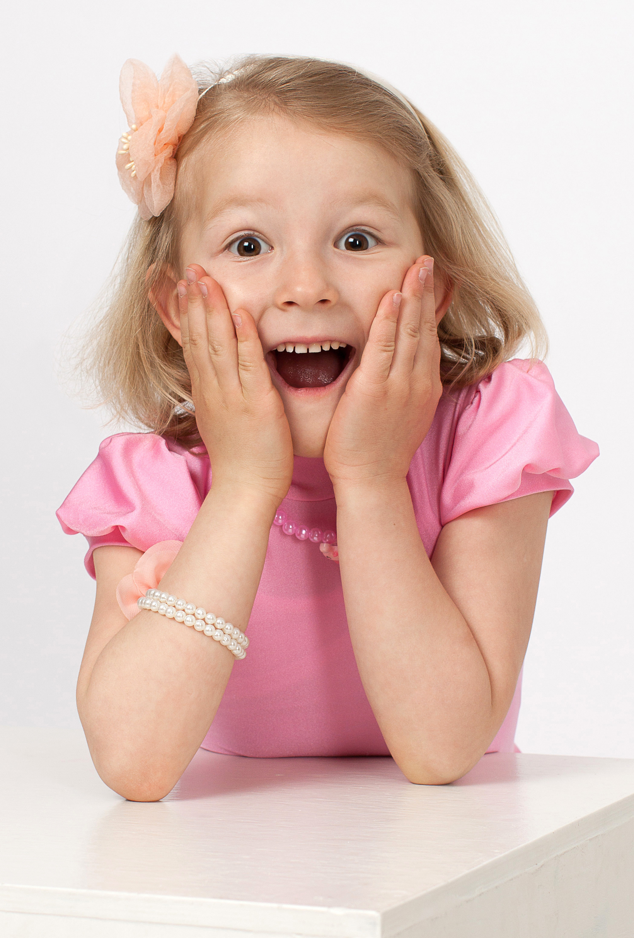 Девочка в розовом платье с эмоцией удивления по грудь на белом фоне.