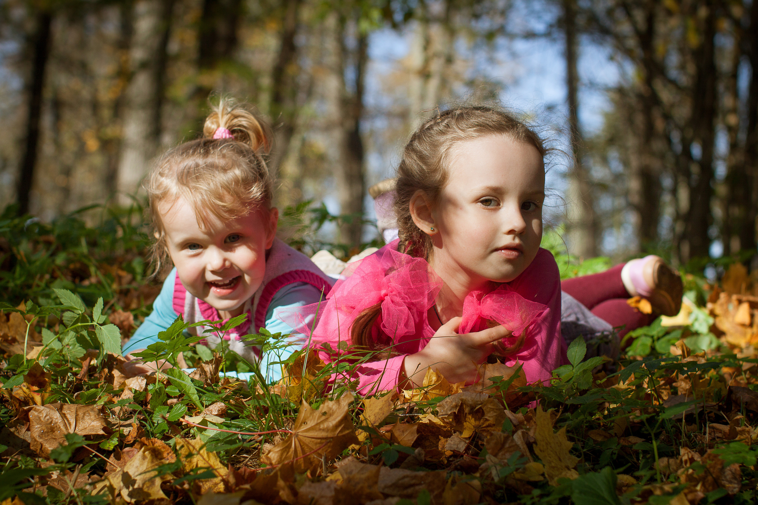Две девочки лежат на осенних листьях в парке.