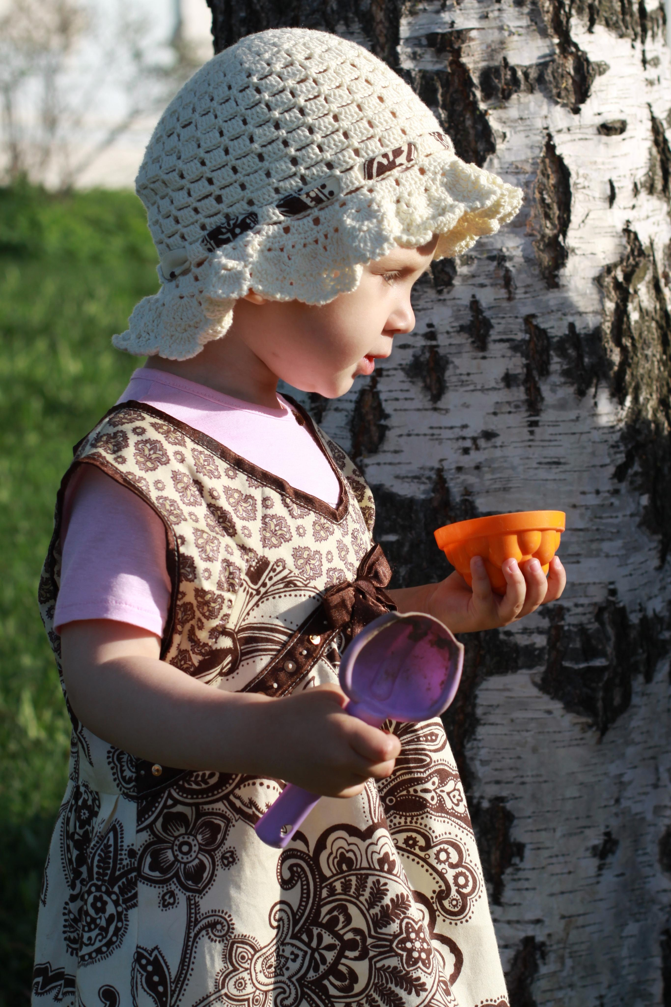 Девочка в вязаной шапочке стоит у березы