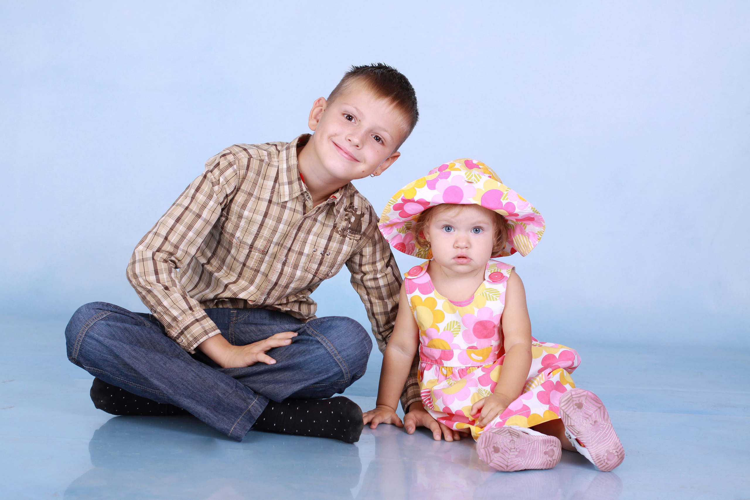 Мальчик с девочкой сидят на голубом фоне в фотостудии.