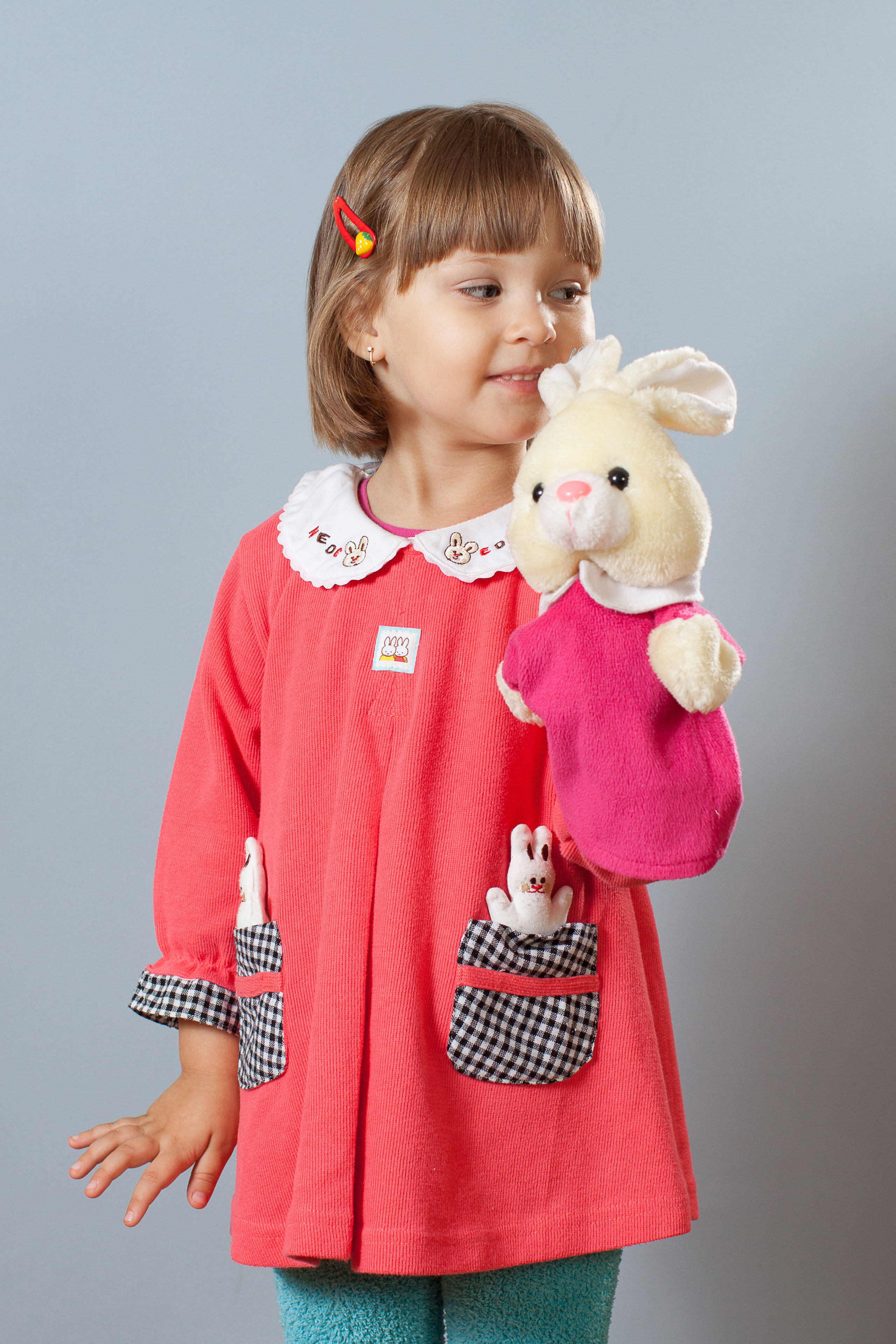 Девочка в красном платье с игрушкой в руке на сером фоне.