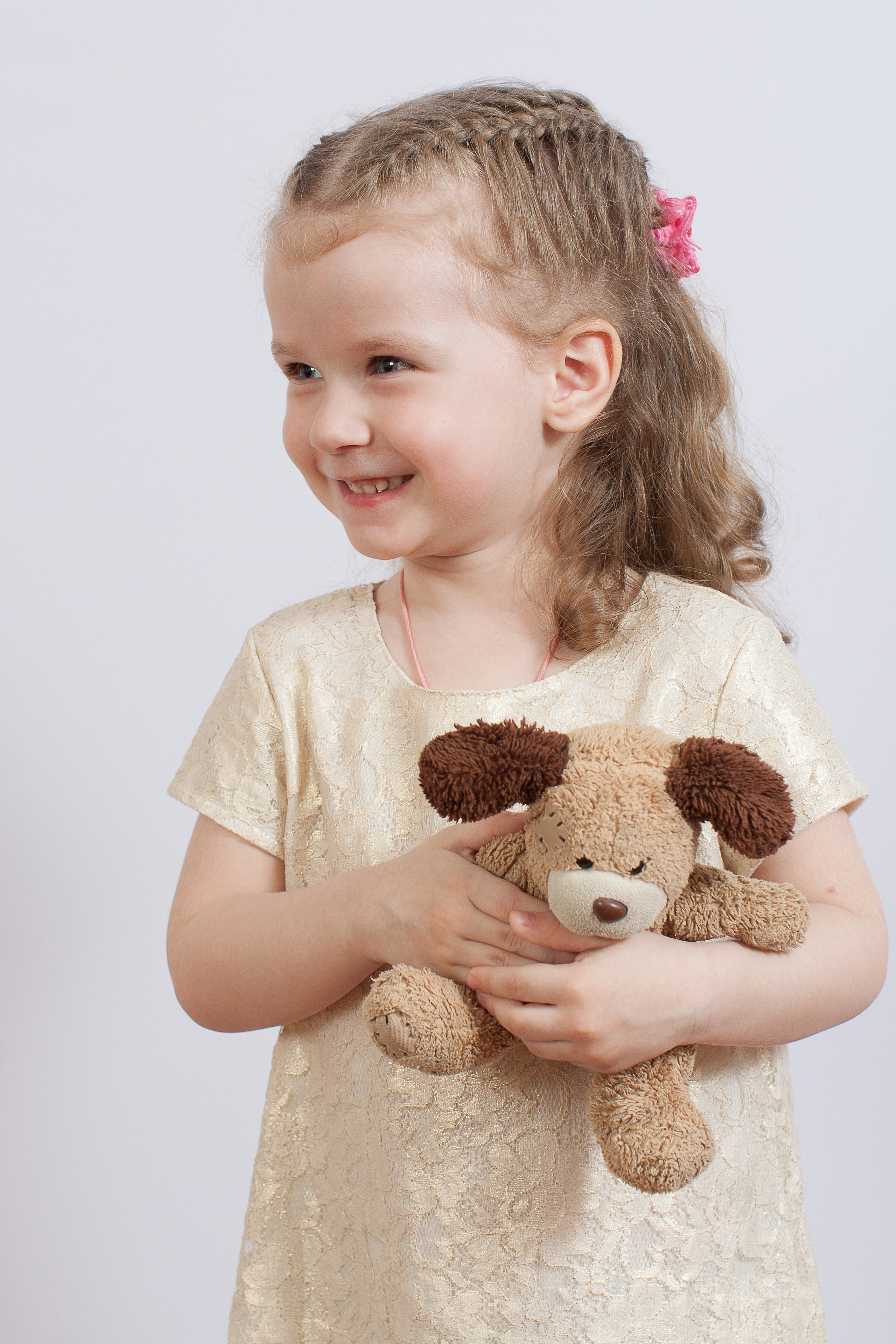 Портрет девочки в светлом платье с мягкой игрушкой в руках на светлом фоне.