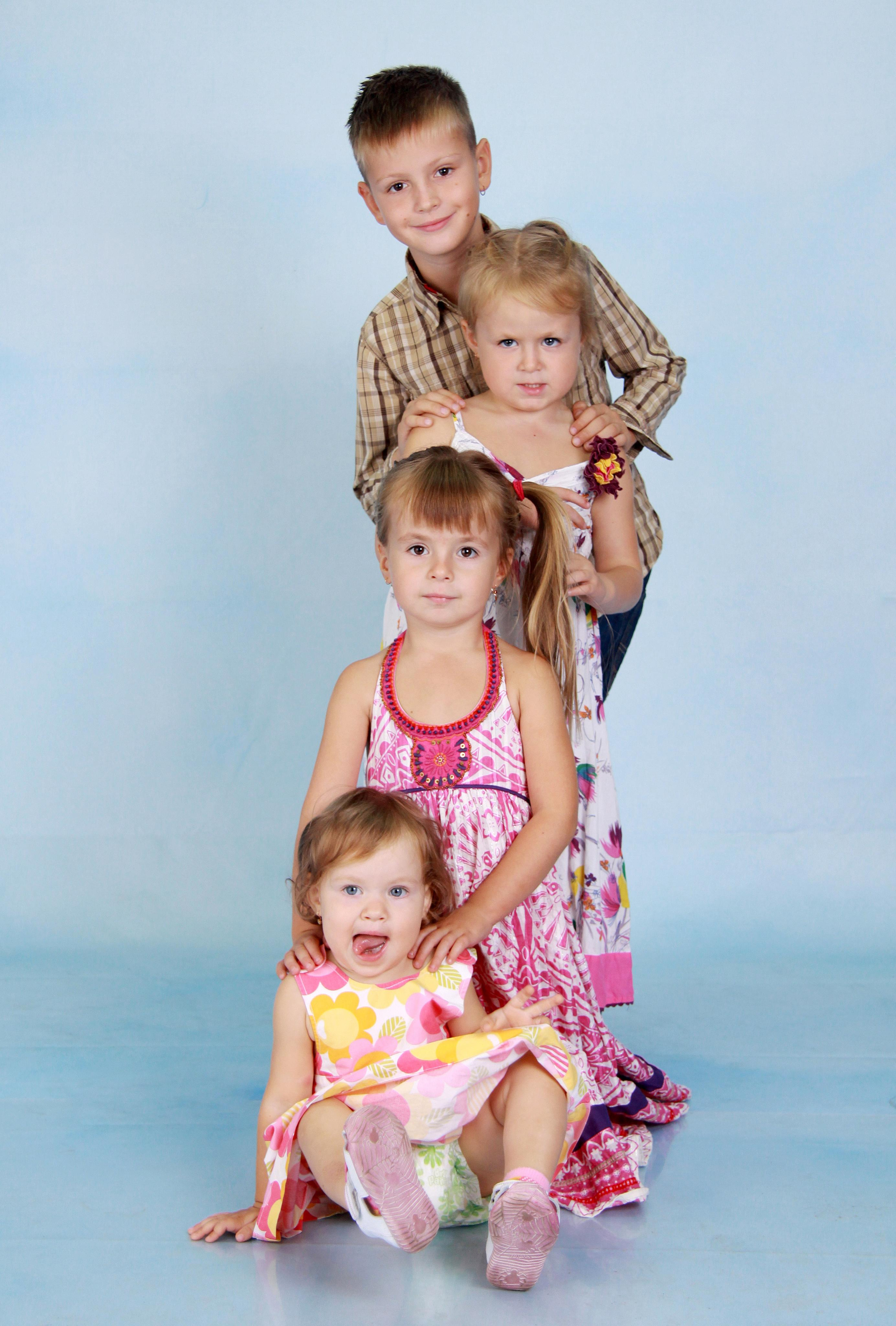 Четыре ребенка стоят друг за другом лесенкой на фоне голубого студийного фона.