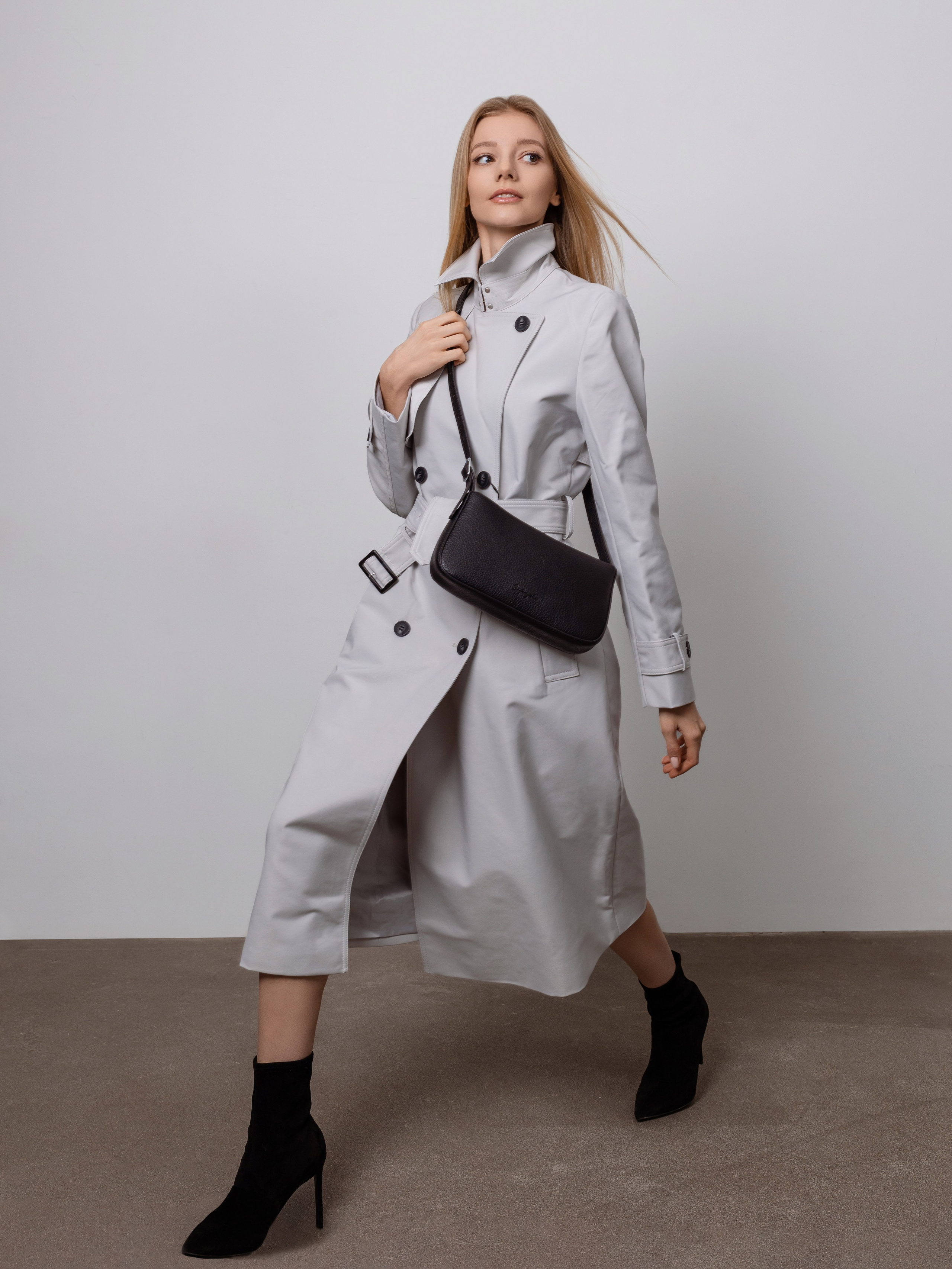 Девушка в белом плаще и с черной дамской сумочкой перекинутая через правое плечо.