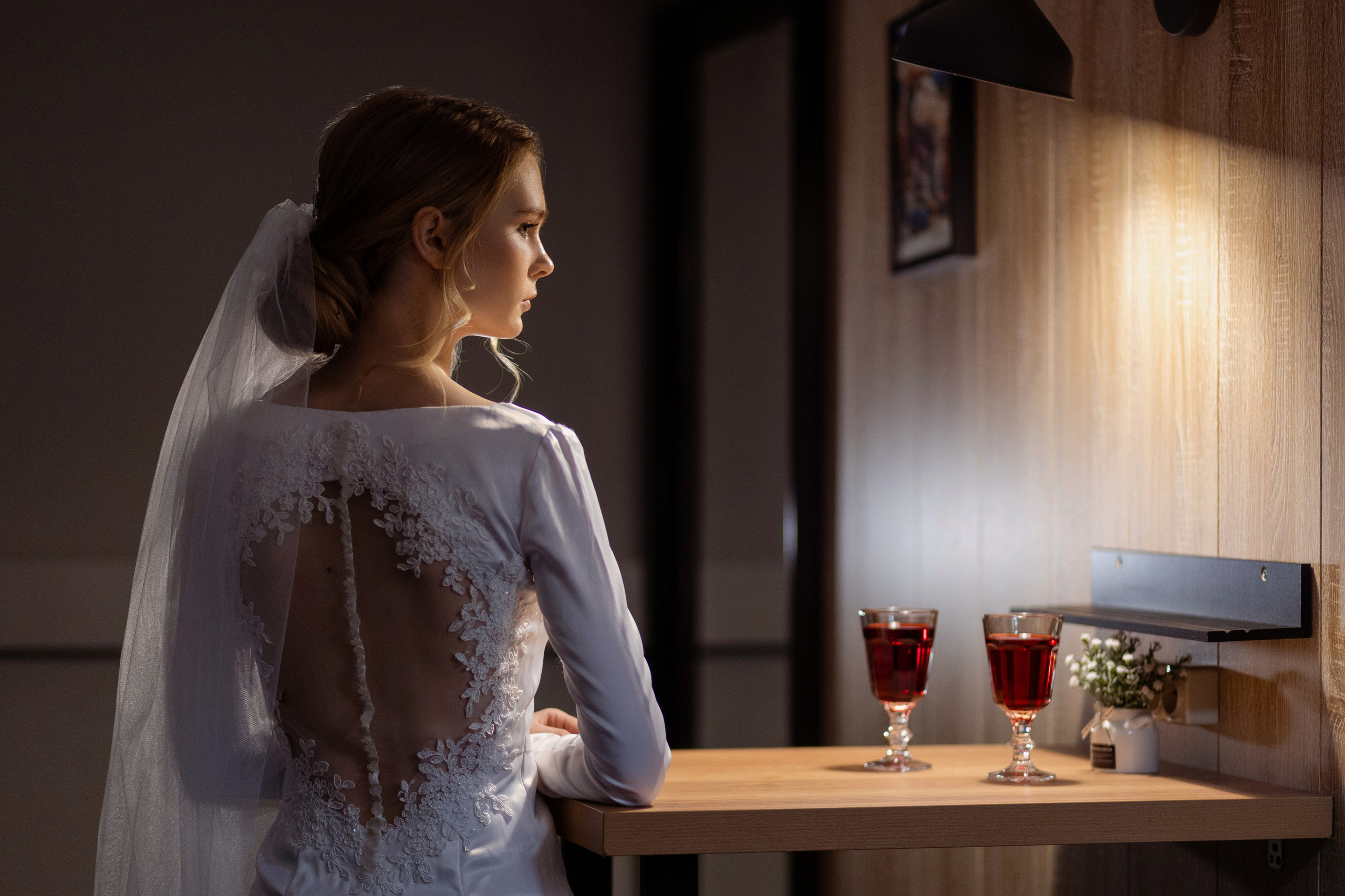 Невеста стоит в пол оборота у стола, на котором стоят бокалы.
