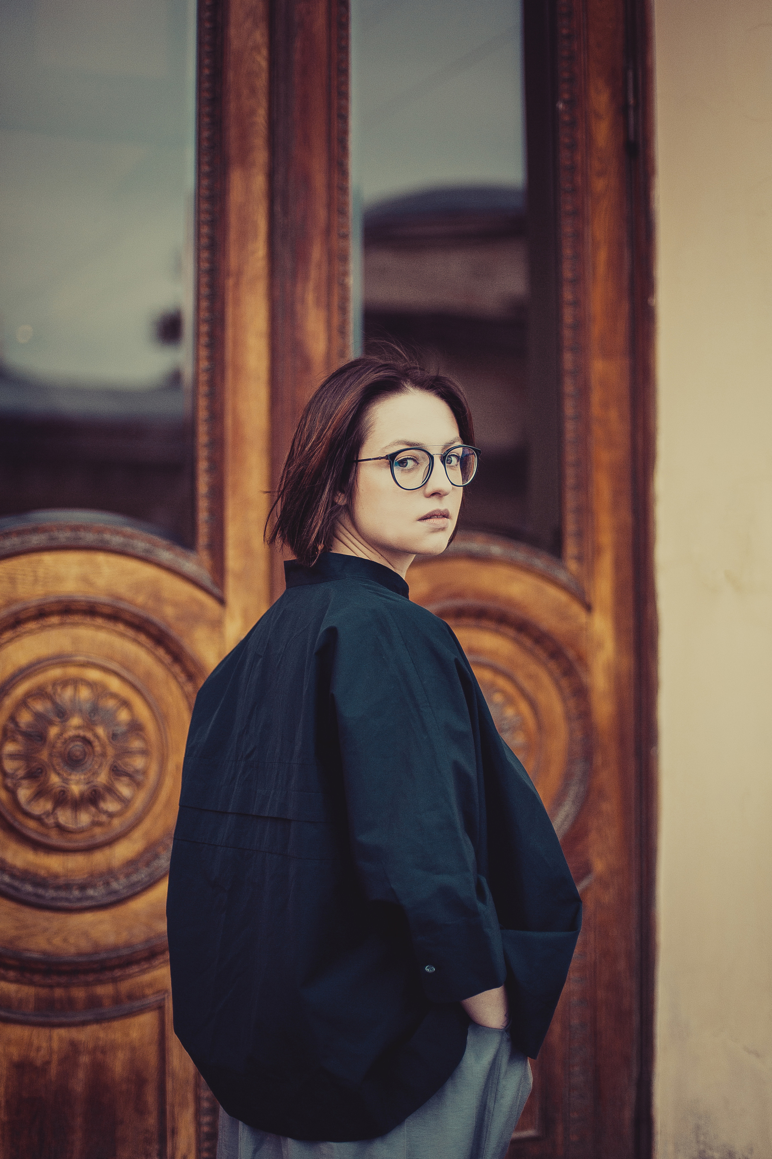 девушка в черной блузке стоит обернувшись около деревянной двери 