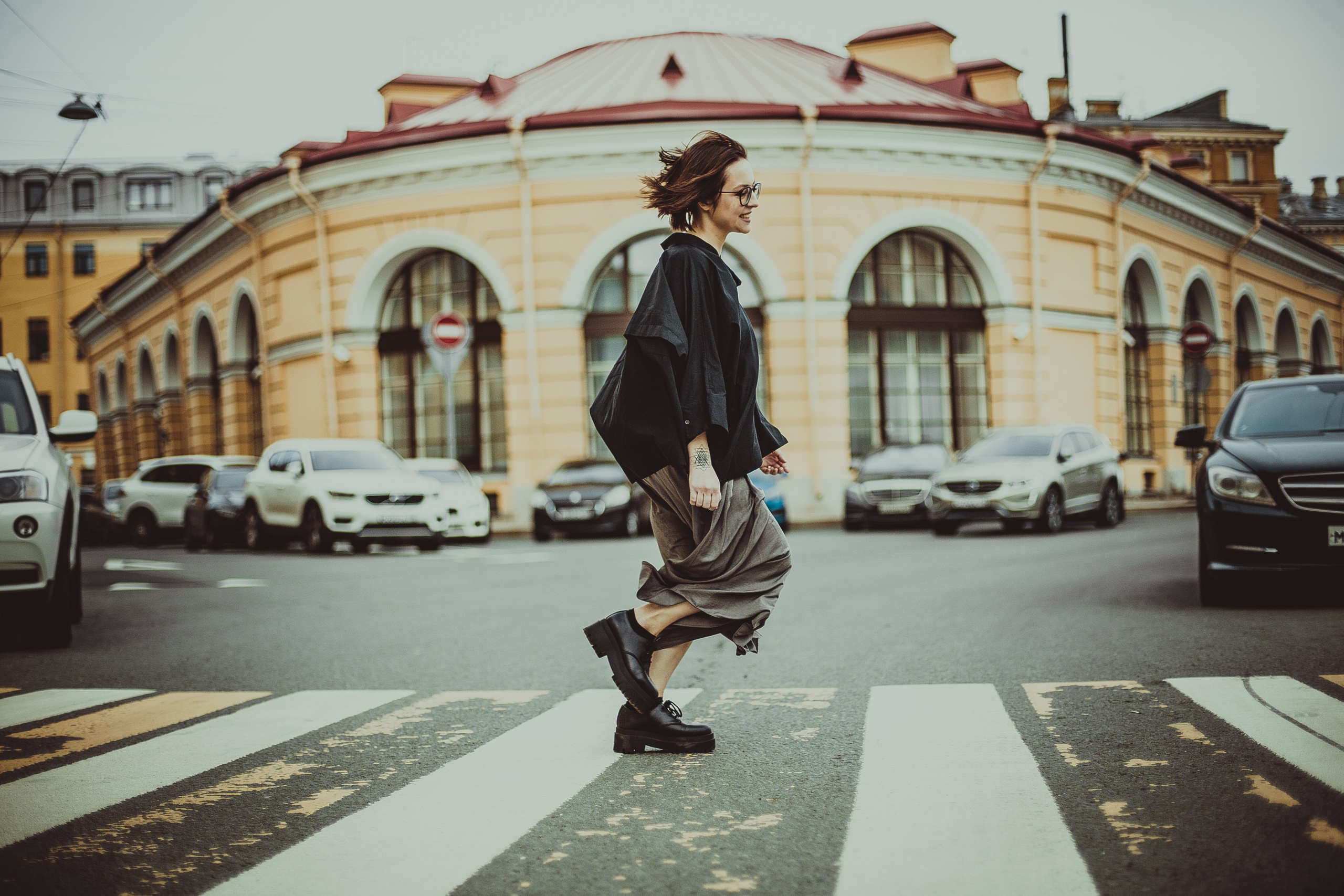 девушка в очках с татуировкой на руке перебегает через дорожный переход