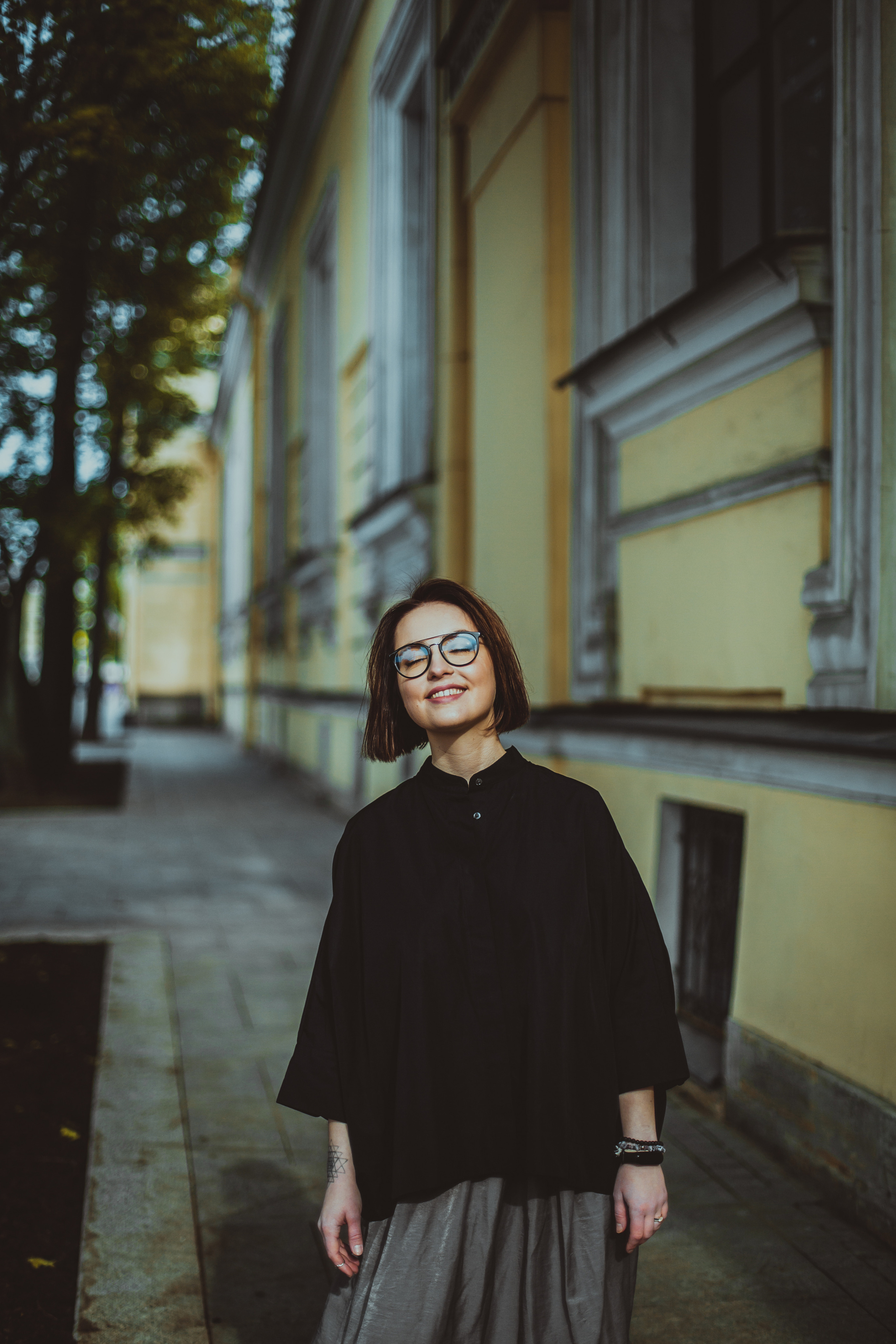 улыбающаяся девушка в круглых очках на улице города