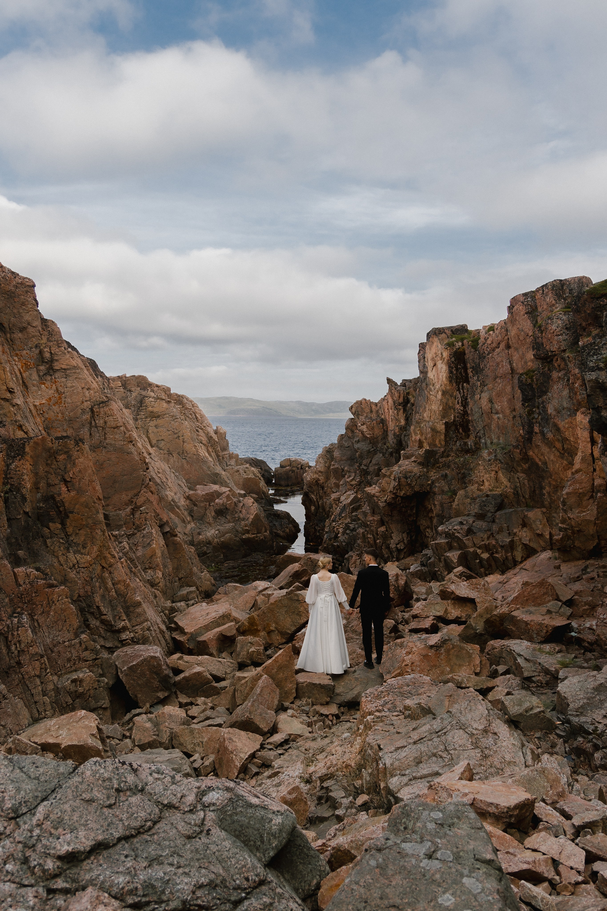 Романтический кадр жениха и невесты, стоящих на скале и смотрящих на закат.