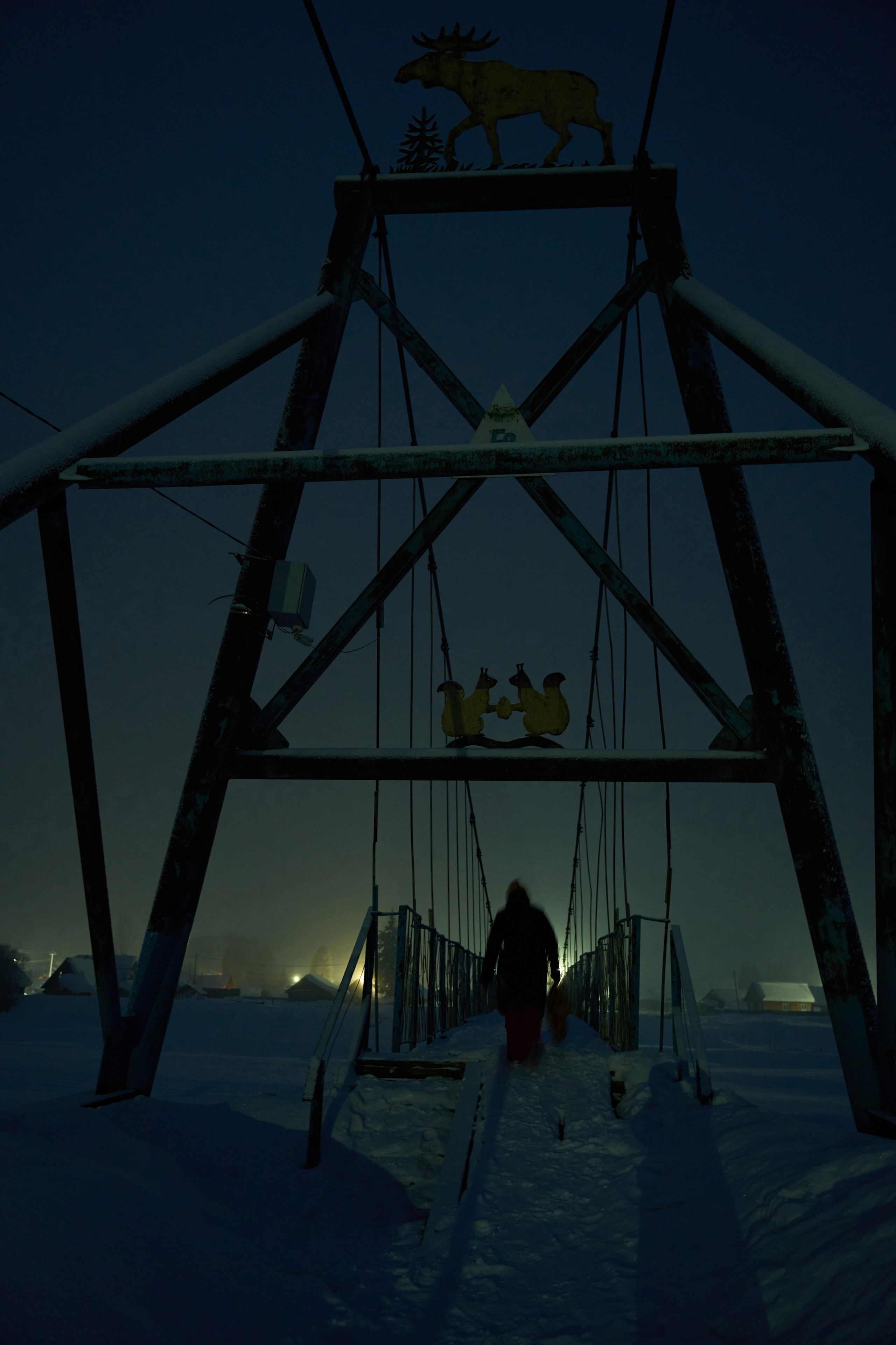 On March 7th, 2025, Lyubov crosses a suspension bridge over the Mras-Su river in Ust-Kabyrza, a remote settelment in the Siberian taiga. Ust-Kabyrza has become the largest remaining settlement in the region, as life in smaller Shor villages grew too harsh to endure. Many have vanished entirely — including Lyubov’s birthplace, the village of Anzas, where no one lives anymore.