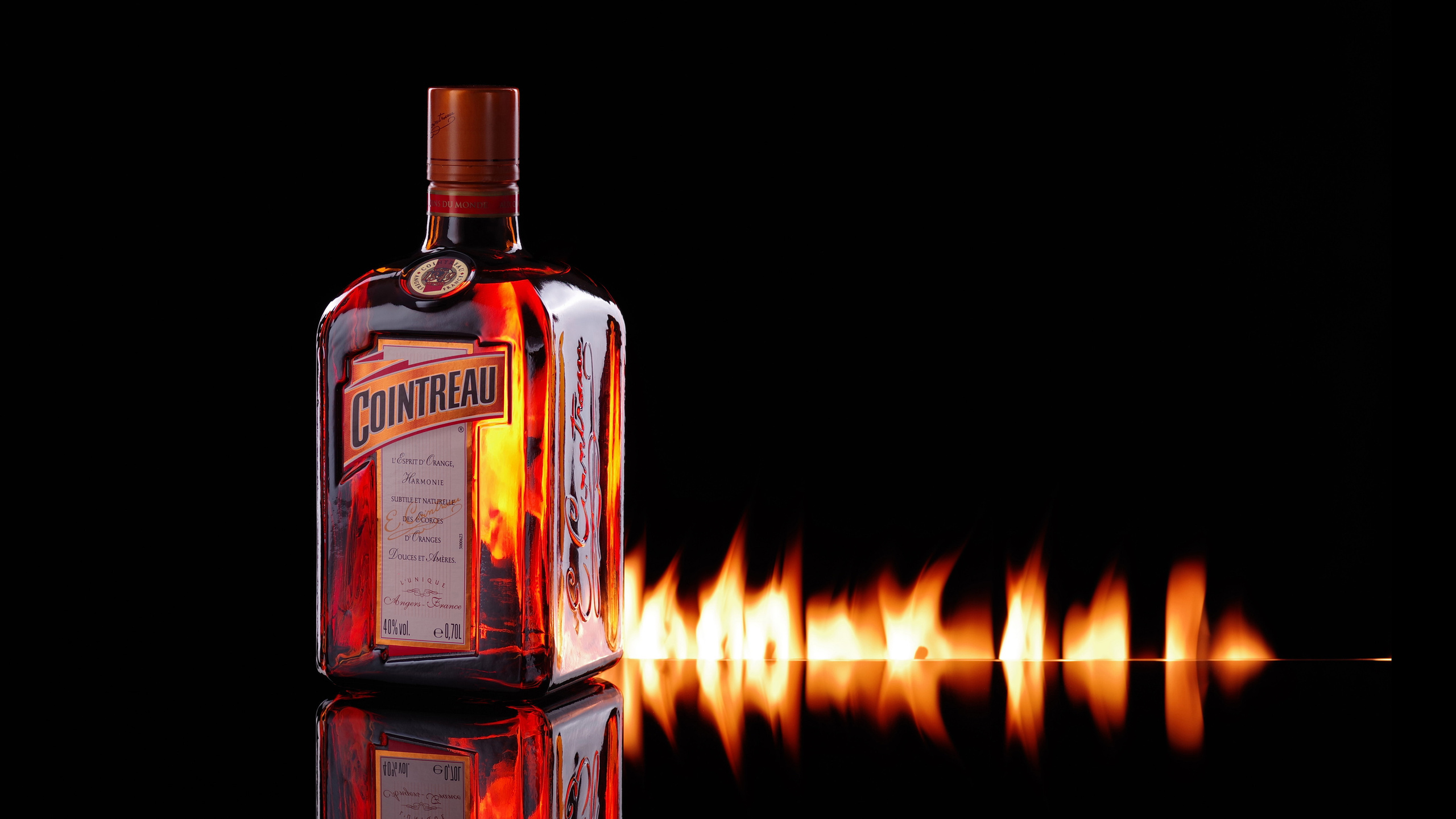 Горящая бутылка ликёра Cointreau на зеркальной поверхности с горящей дорожкой
