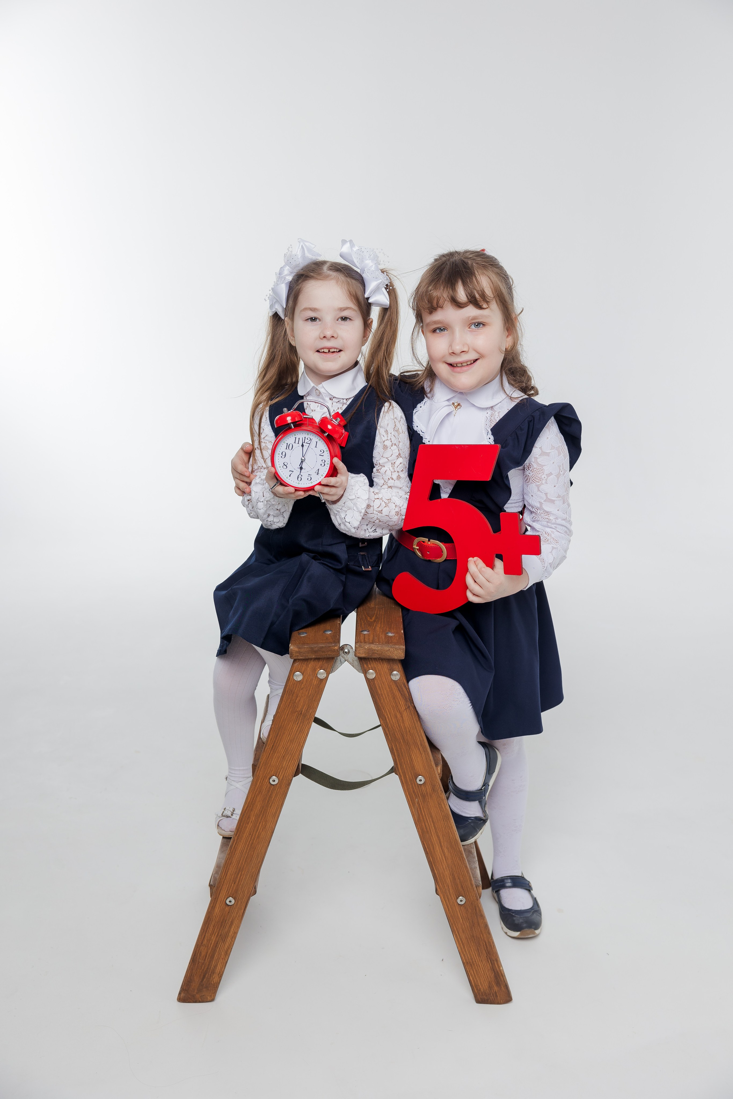 Две девочки сидят на лестнице вместе и держат будильник