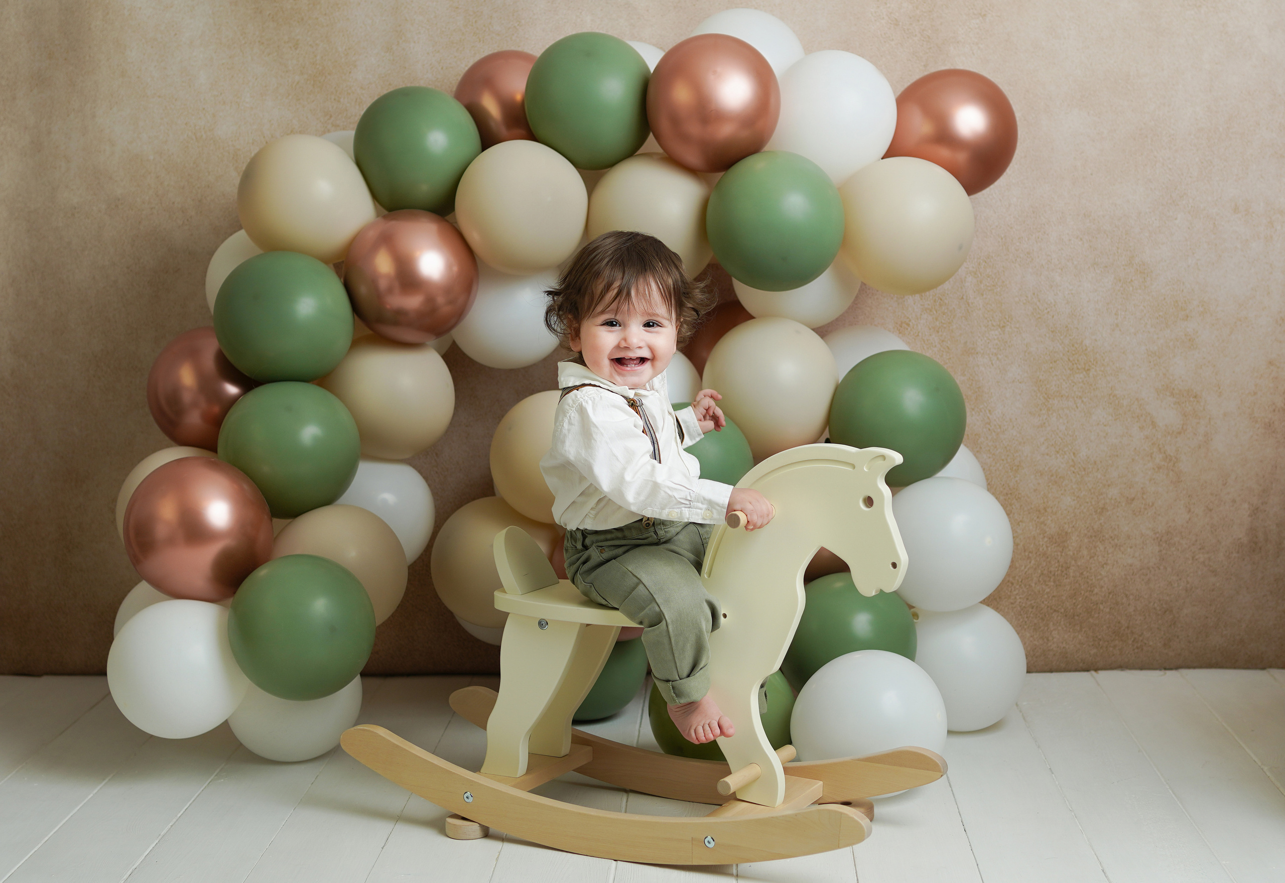 На фото много красивых зеленых шариков, малыш катается на детской лошадке.