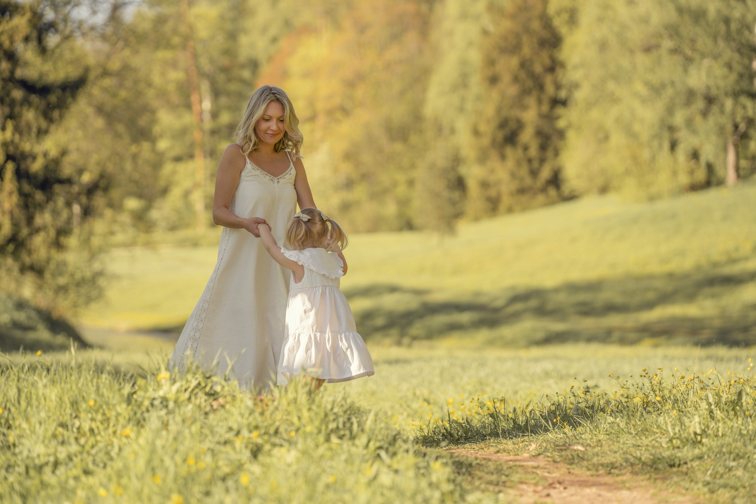 Мама с дочкой кружатся и играют на полянке в Павловском парке. Они одеты в белые летние платья.