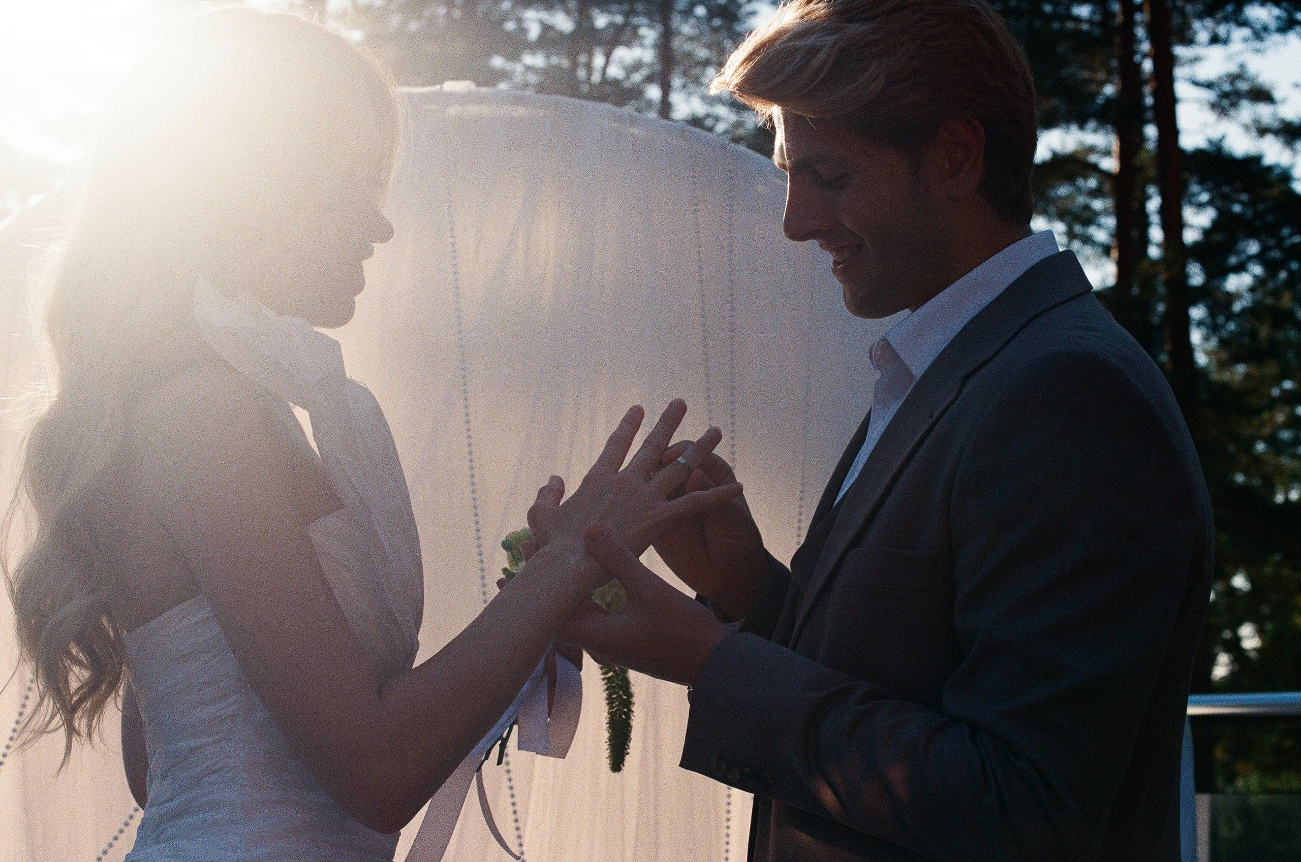 Момент обмена кольцами на выездной церемонии — мягкий контровой свет среди сосен