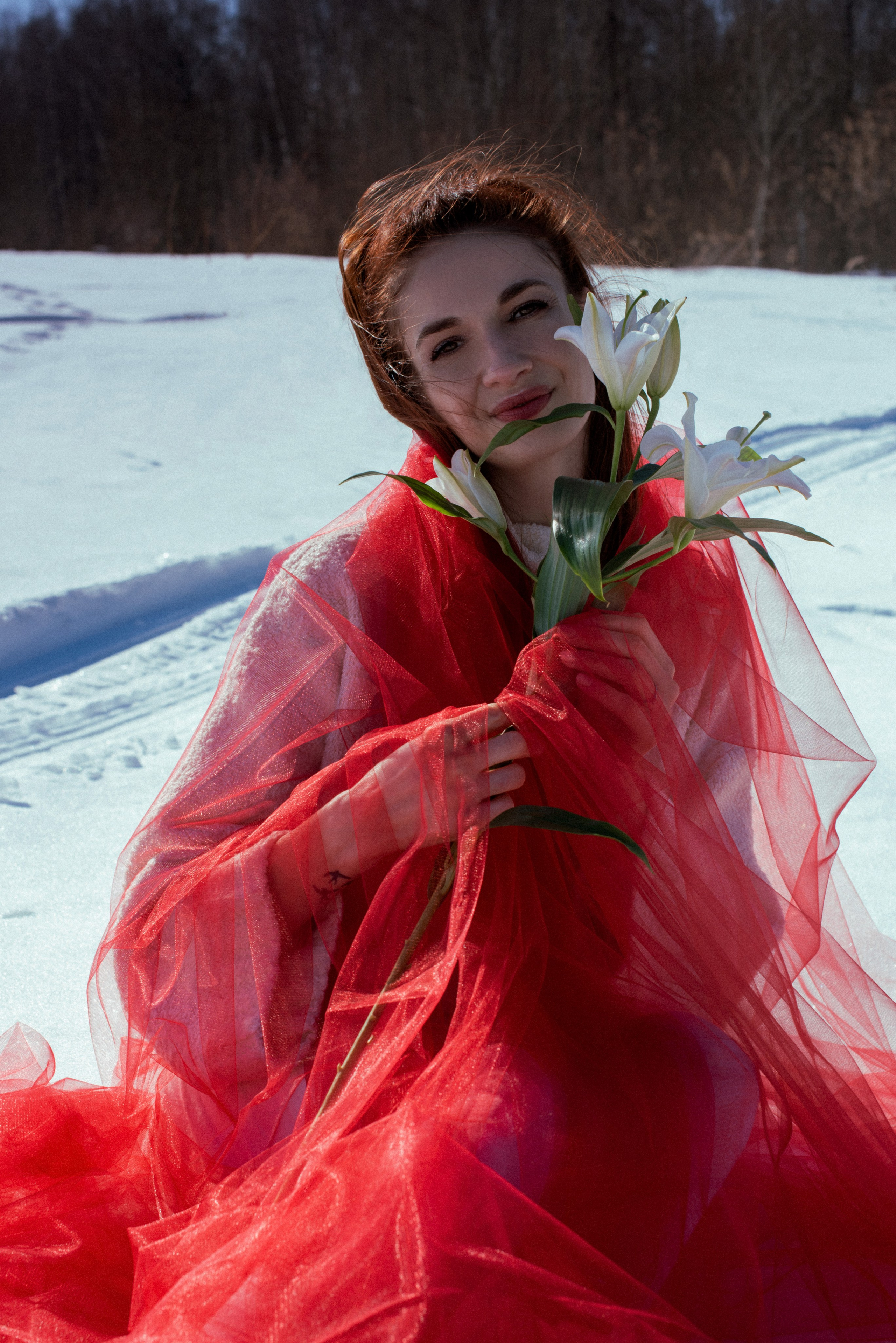 На снегу — девушка, завернувшаяся в красный фатин, под ним белый свитер.