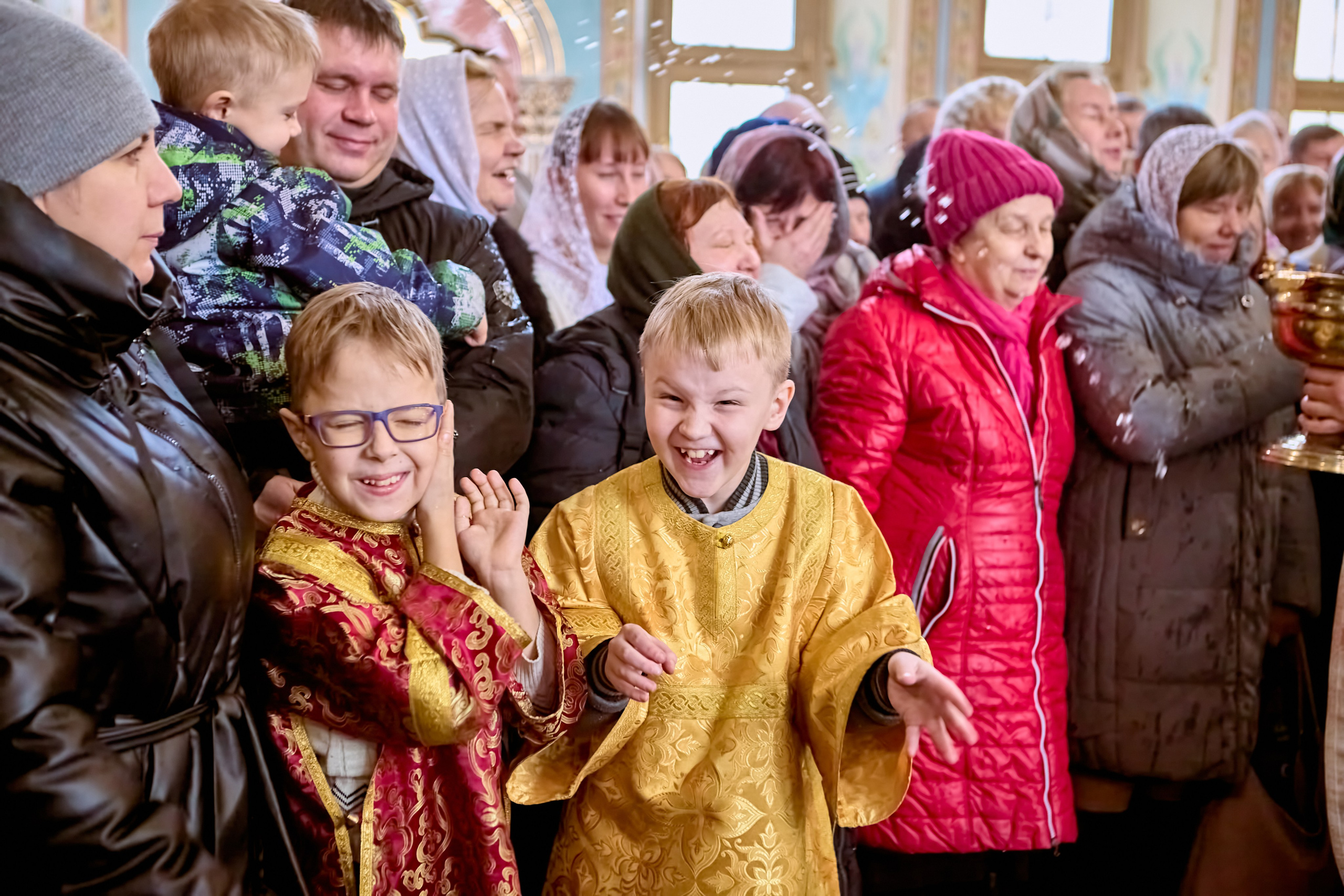Двое мальчишек в веселых эмоциях от окропления крещенской водой в день праздника Крещения Господня