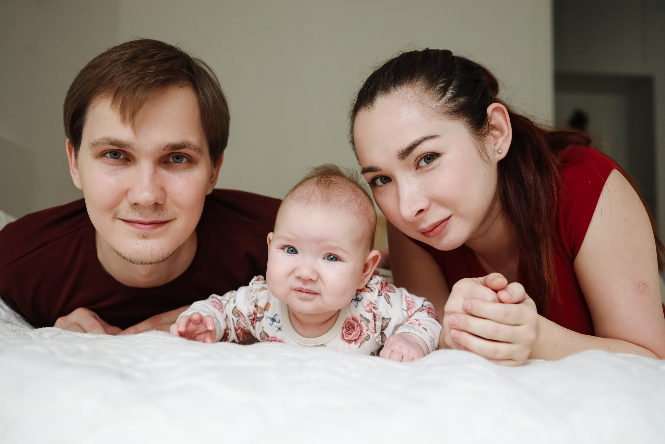 Мама папа и младенец смотрят в кадр на кровати