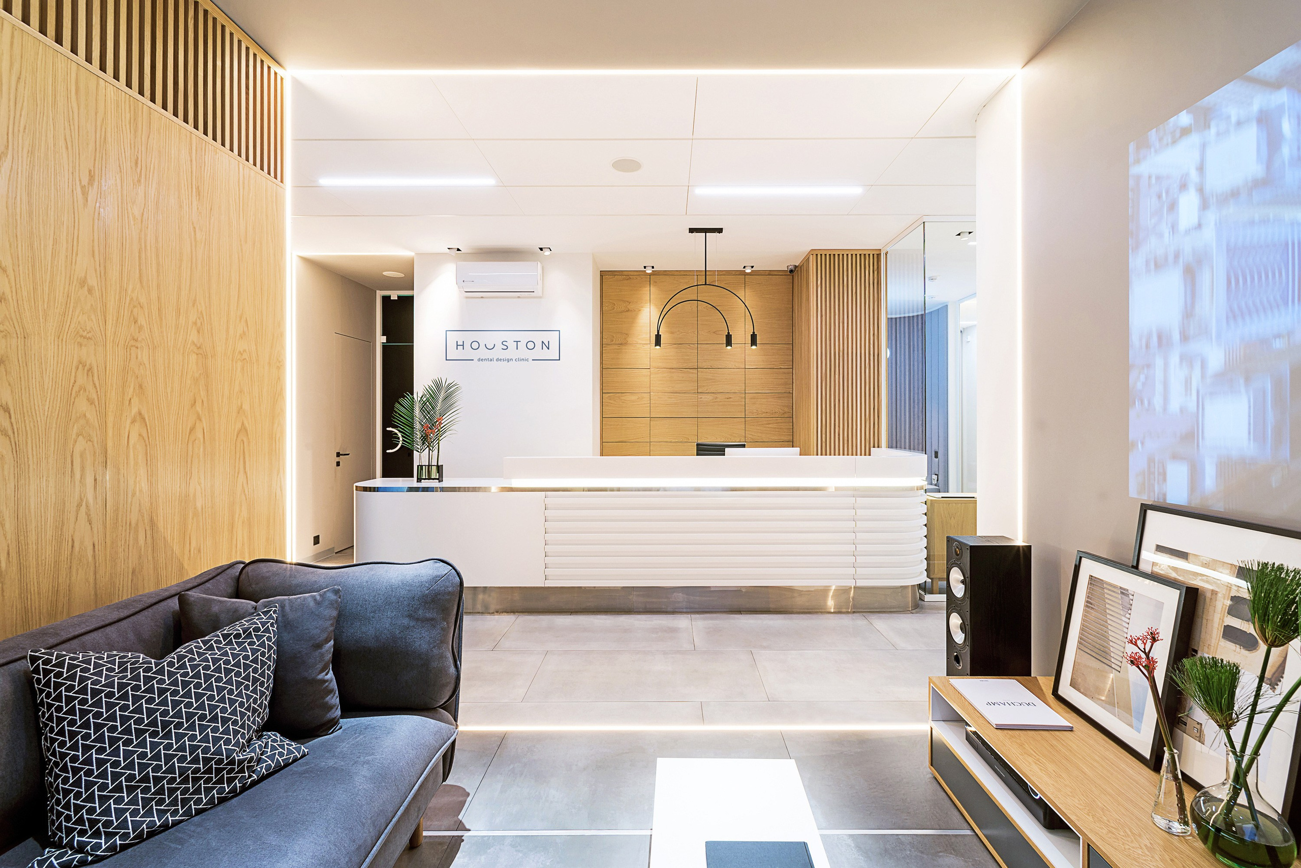 дизайн интерьера стоматологической клиники выполнен в современном минималистичном стиле с теплой домашней атмосферой. Текстуры дерева, наливной пол, яркие акценты, чистота линий, модульная сетка, стеклянные перегородки