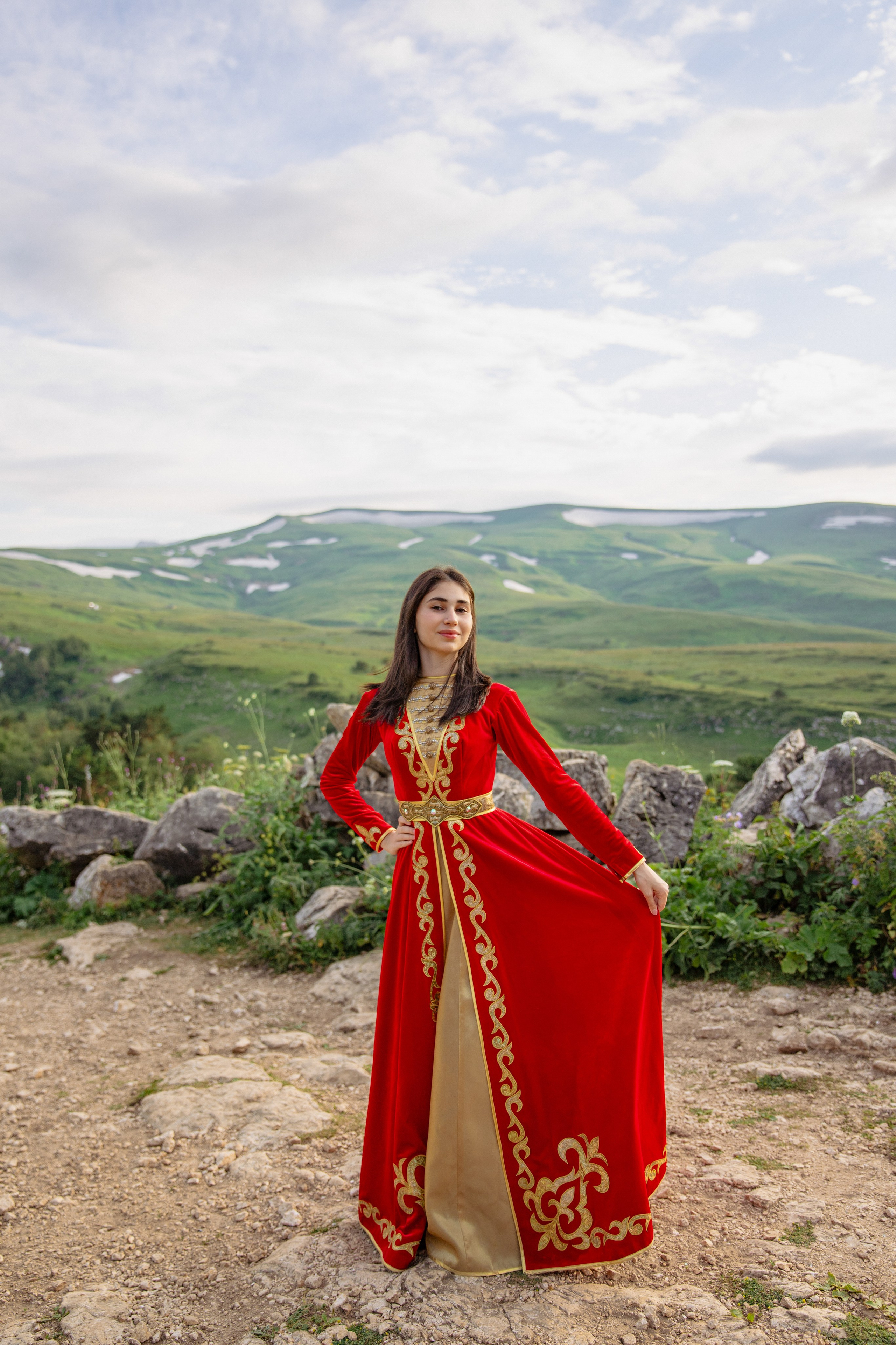Молодая девушка в адыгейском национальном костюме, позирующая на фоне живописных гор.