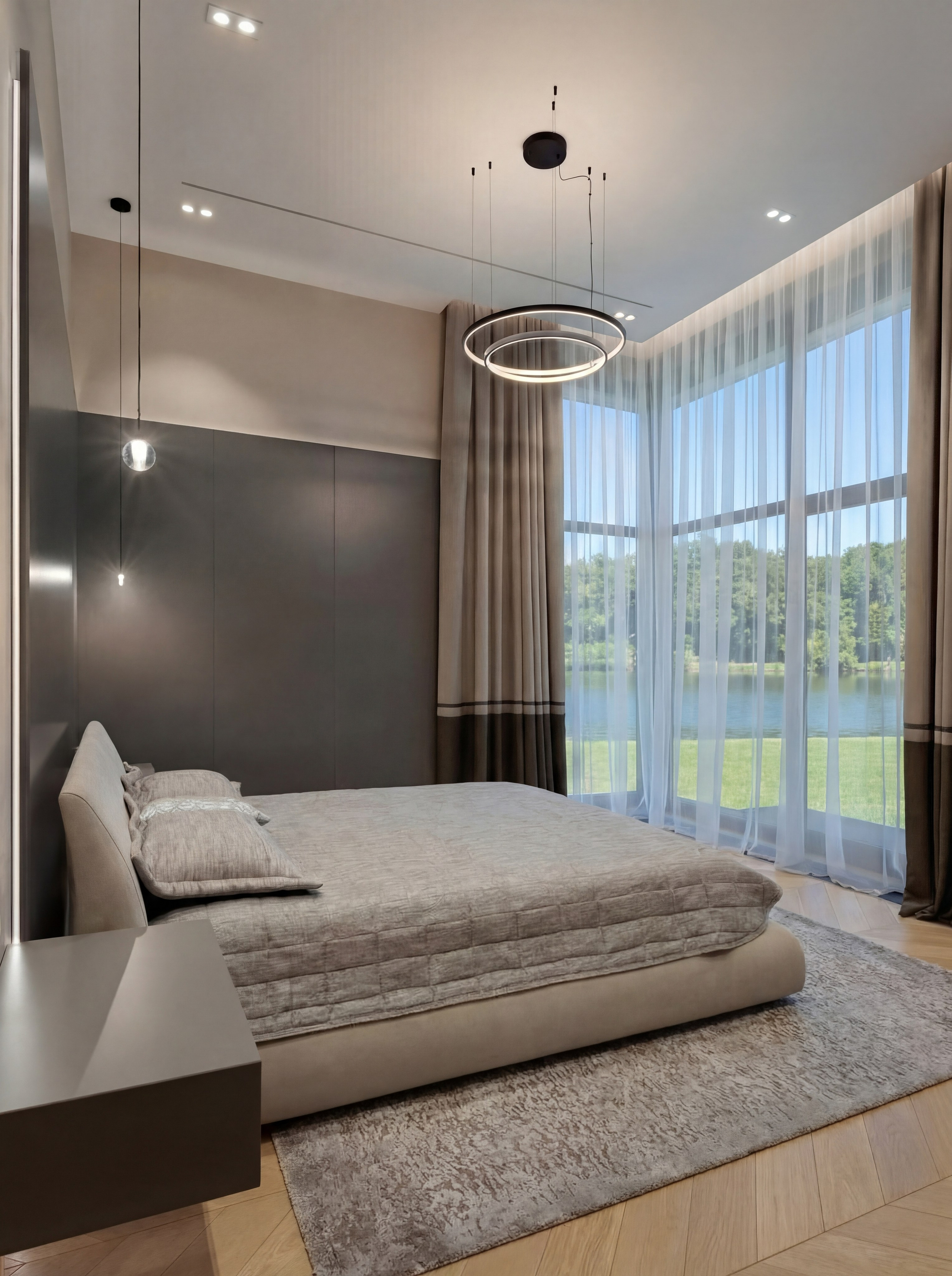 Современная спальня от Валерии Котович в доме у воды: двусветное панорамное окно с видом на озеро, кровать в серо-бежевых тонах, темные стеновые панели и дизайнерская кольцевая люстра.