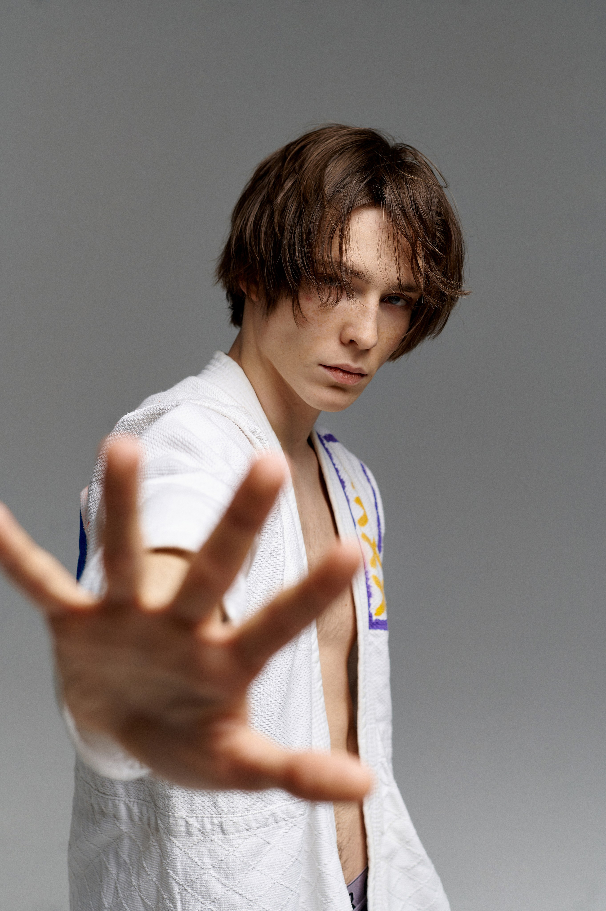 Парень модель с рукой в кадре стоит на сером фоне