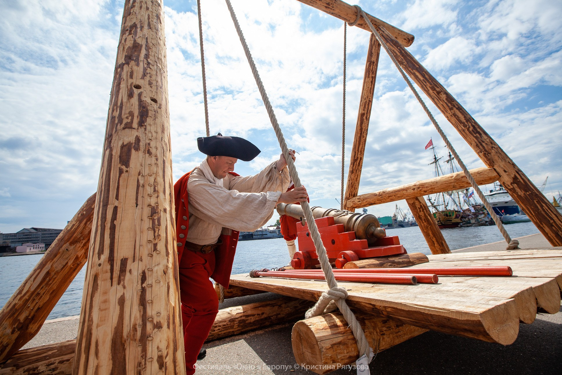 Герой исторического фестиваля "Окно в Европу" в Санкт-Петербурге раскачивает конструкцию с пушкой. Фото в полный рост на фоне Невы.