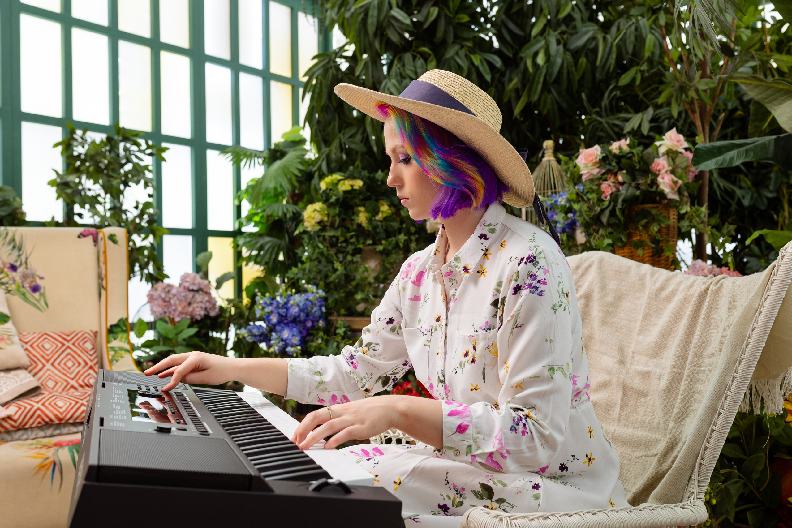 На фоне зеленых насаждений за пианино сидит девушка в шляпке.