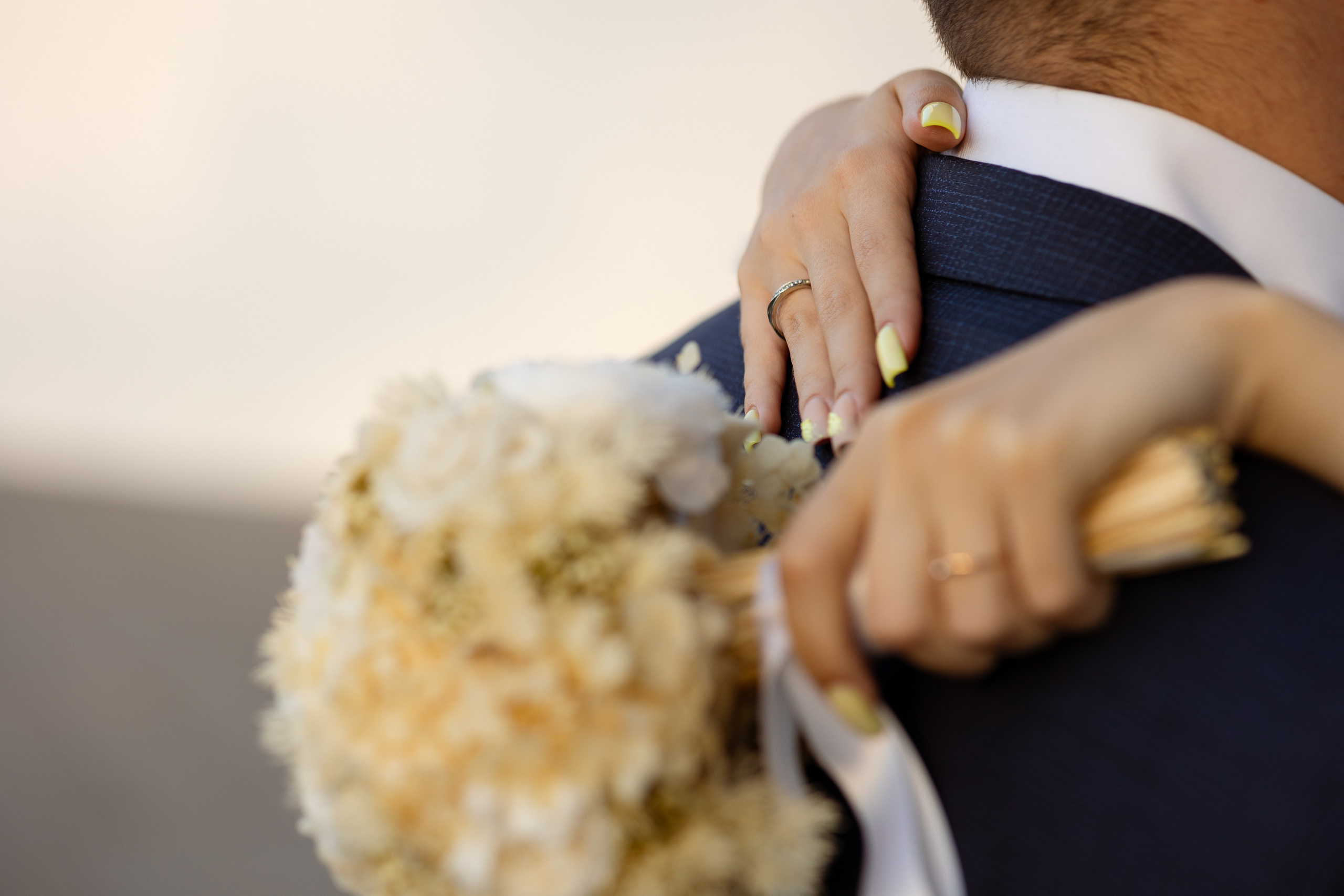 Невеста обнимает жениха. В левой руке молодой букет