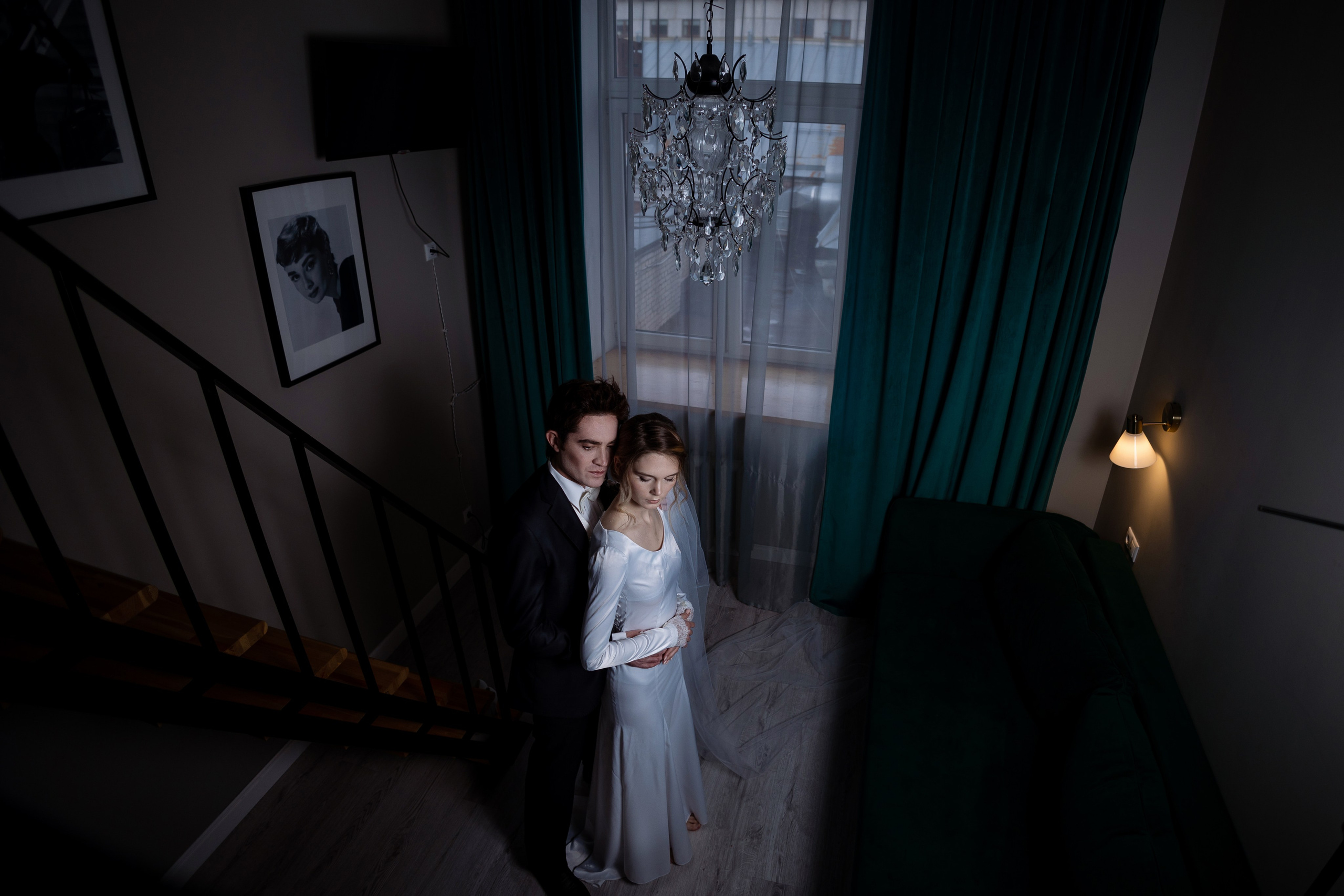 Жених обнимает невесту в полумраке у окна.