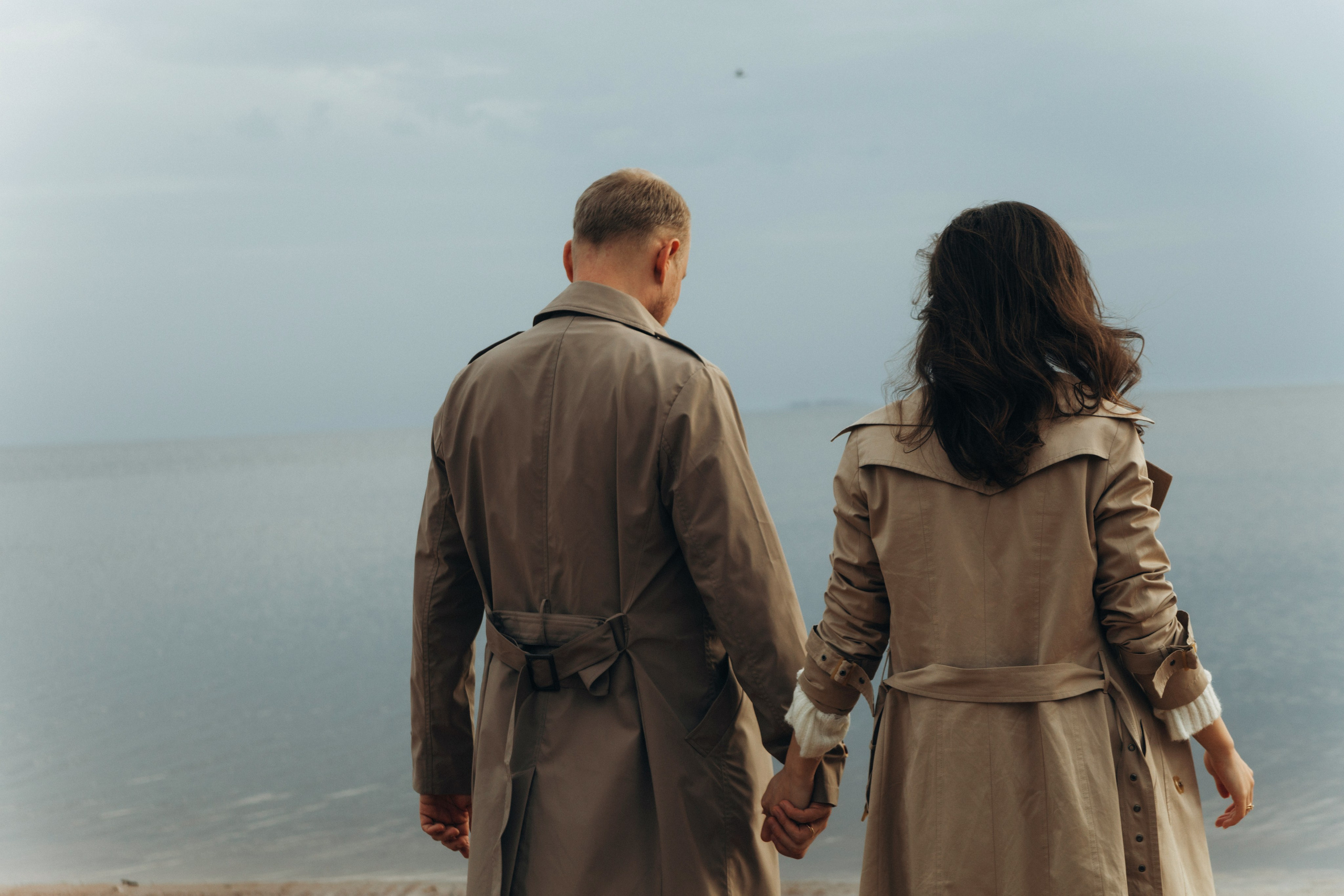 Пара держится за руки на фоне волн Финского залива, закатный свет